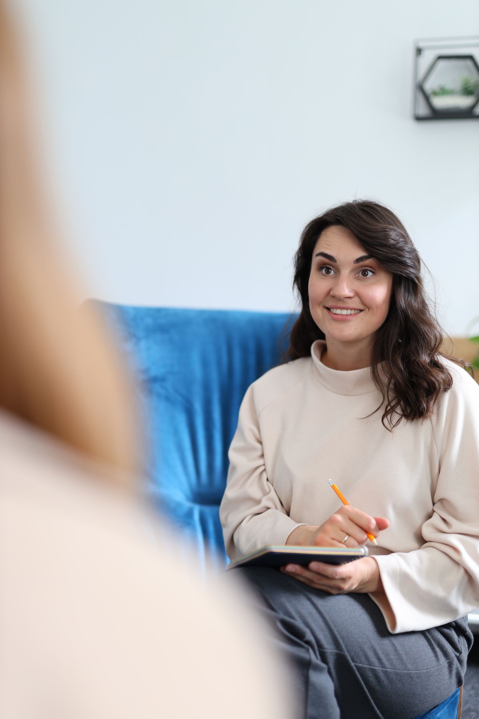 Une femme souriante prend des notes lors d'une réunion sur un canapé bleu.