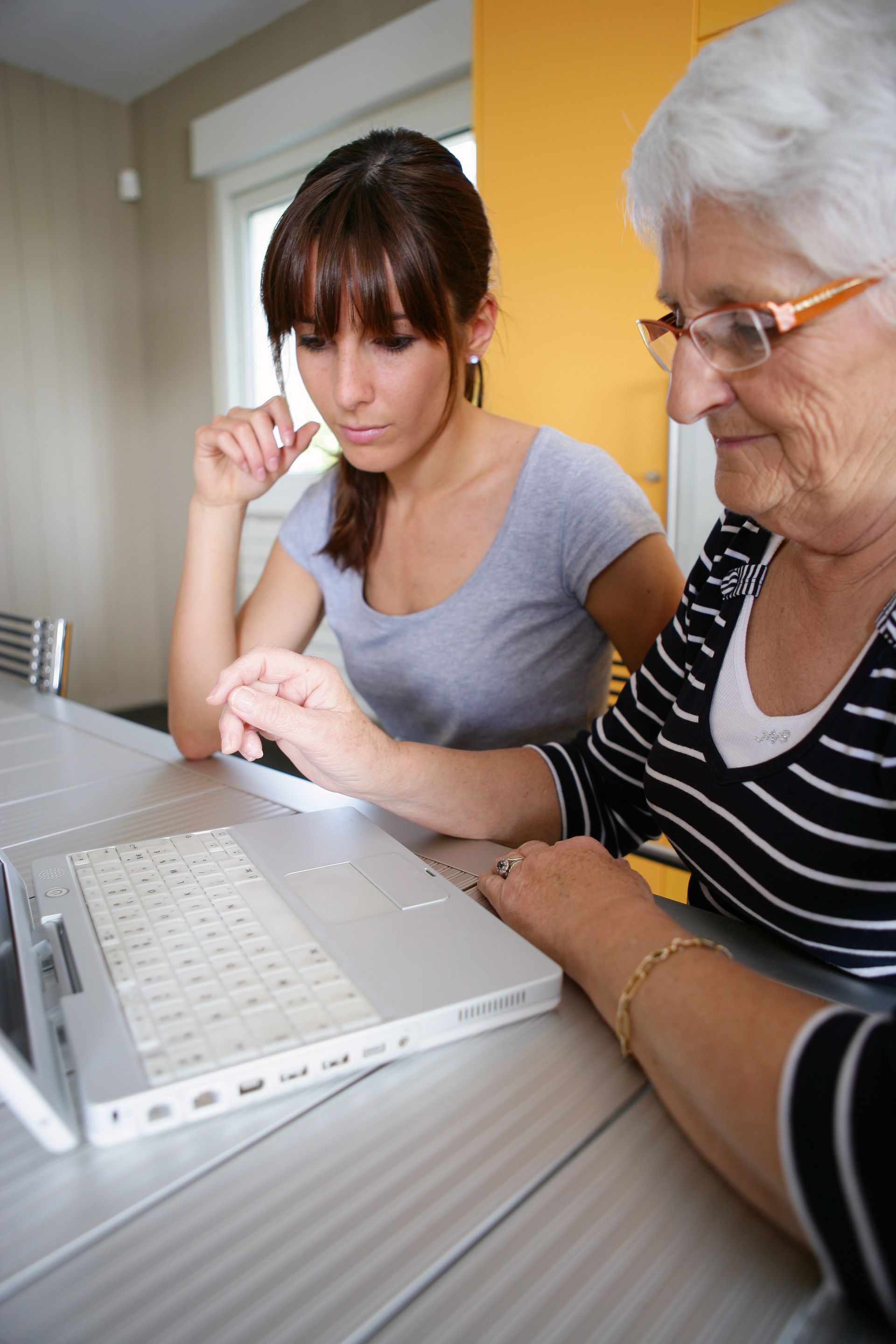 Une jeune femme et une femme plus âgée regardent ensemble un ordinateur portable à une table.