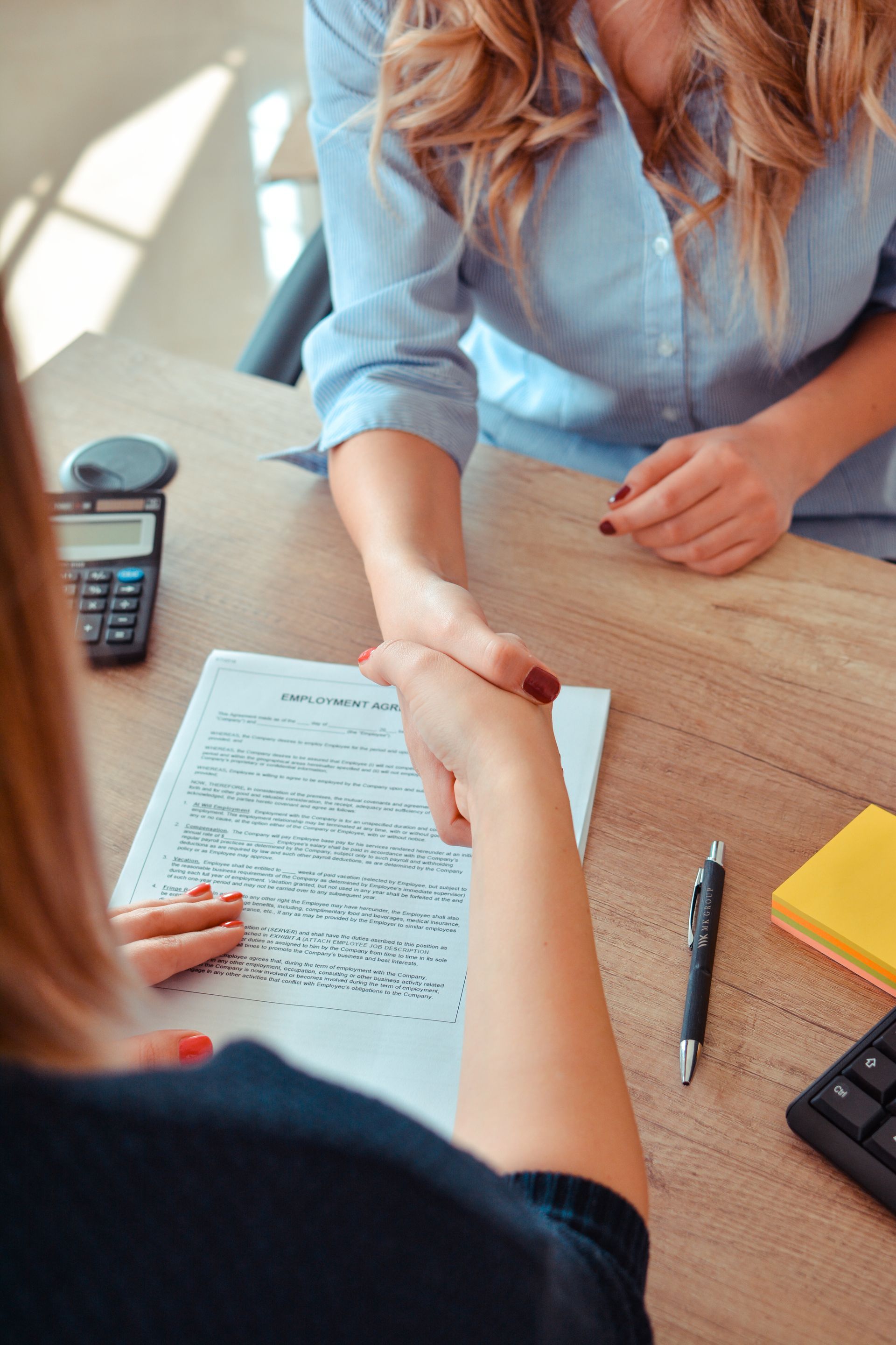 Deux femmes se serrent la main au sujet d'un document sur un bureau, probablement un accord commercial.