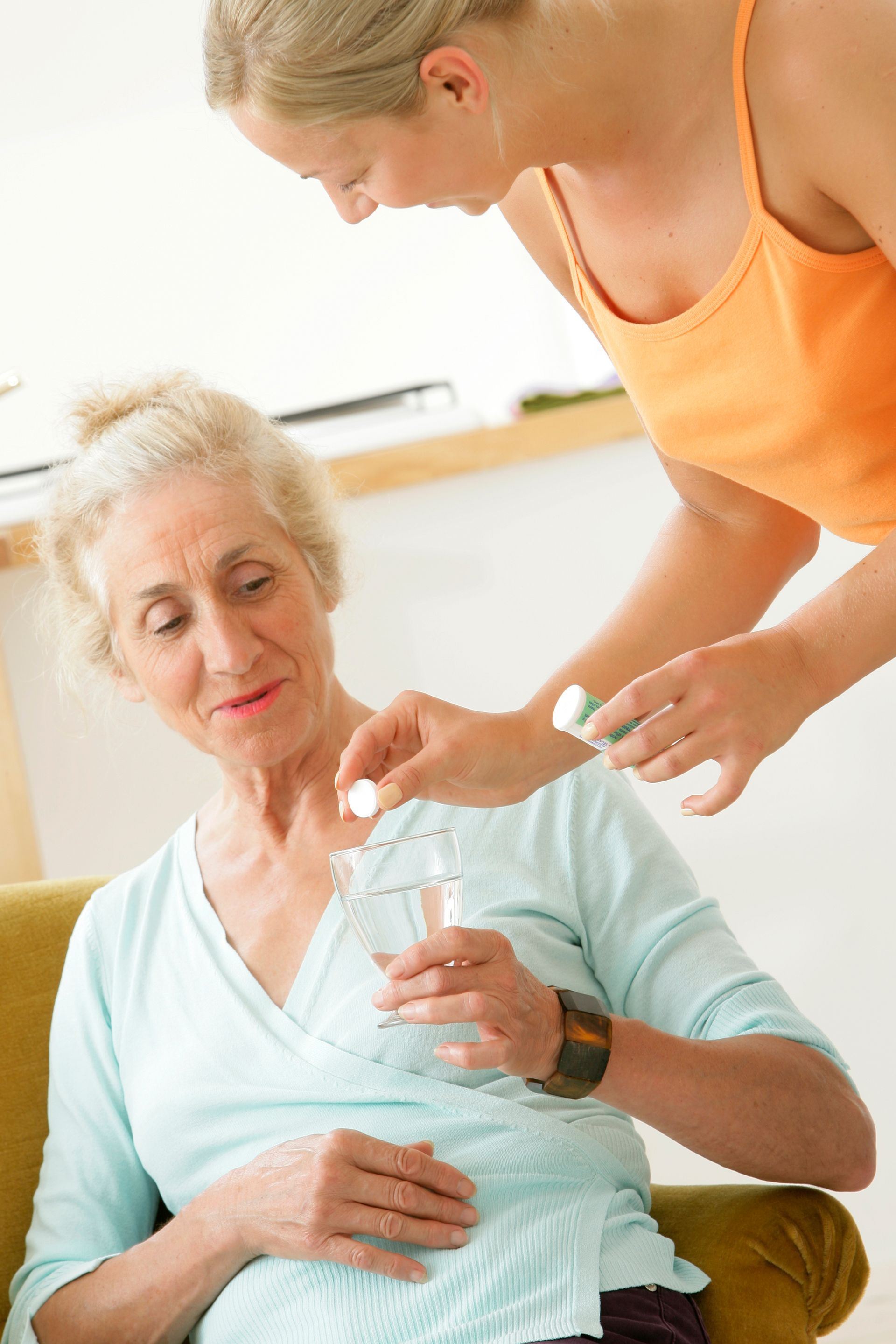Une femme donne des pilules à une femme âgée tenant un verre d'eau.