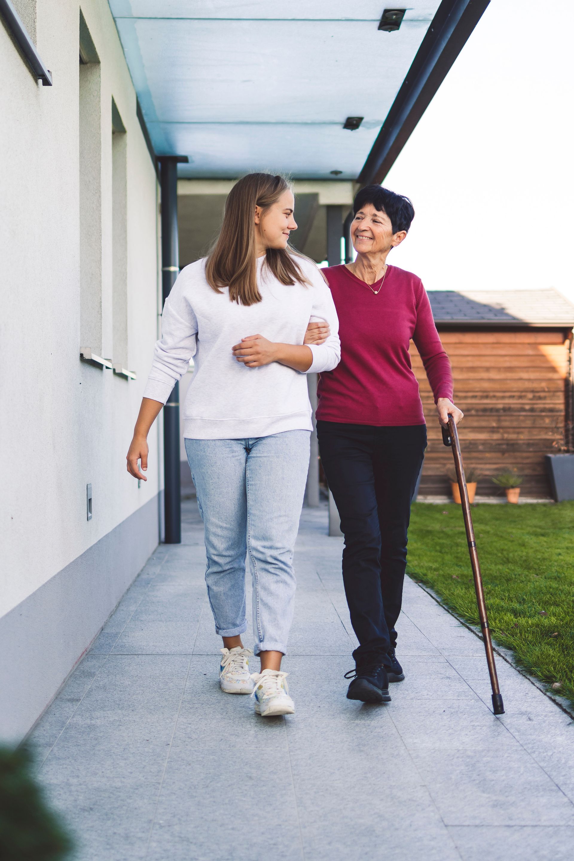Une jeune femme aide une femme âgée à marcher dehors ; toutes deux sourient.