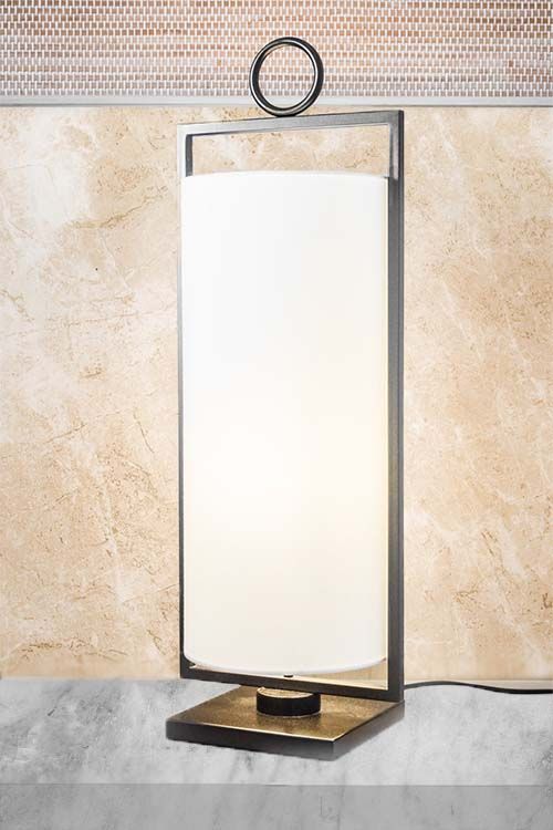 Una lámpara de mesa con pantalla blanca está colocada sobre una mesa frente a una pared.