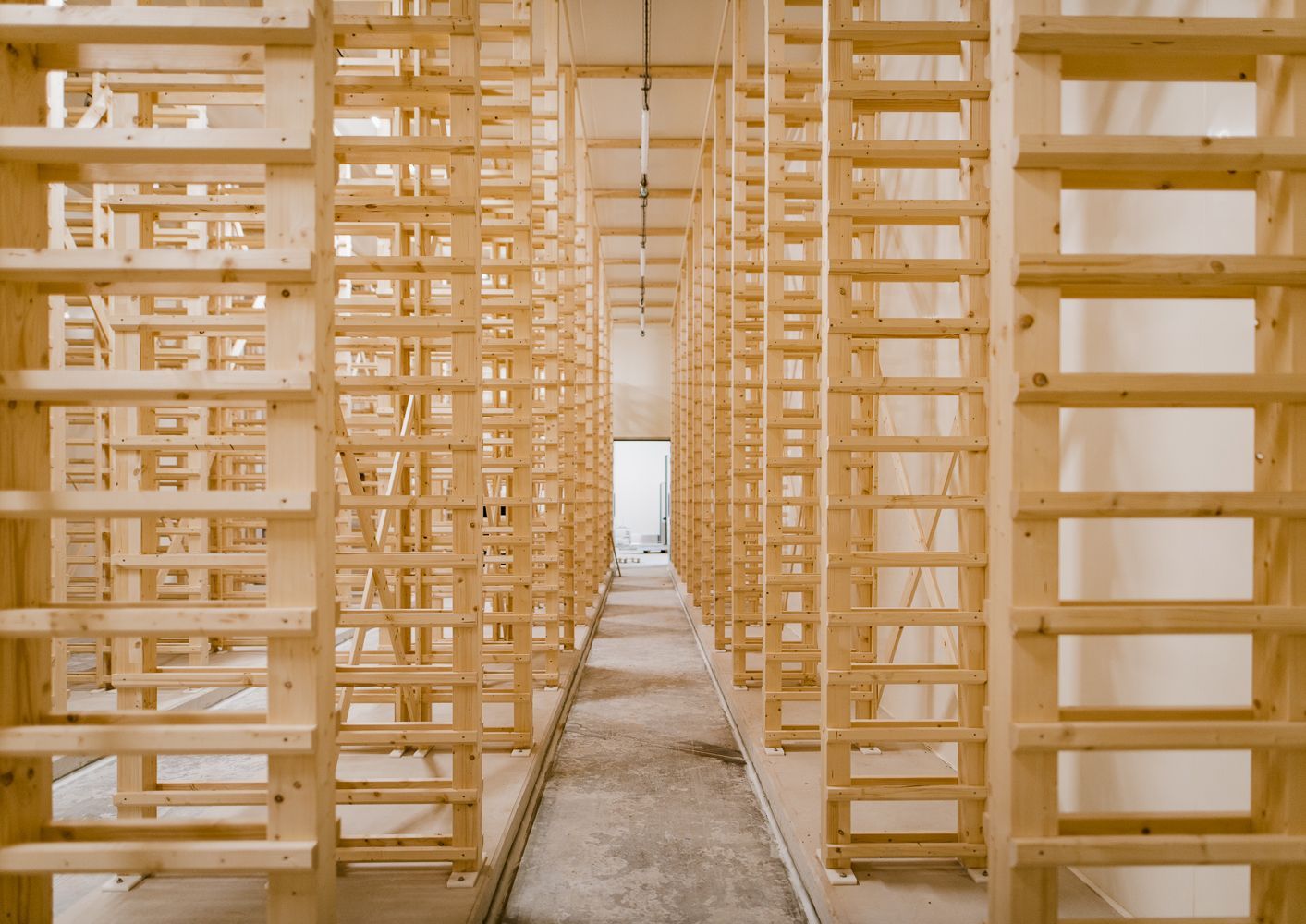 Des rangées d'étagères en palettes de bois dans un entrepôt, créant des allées menant à une porte lumineuse