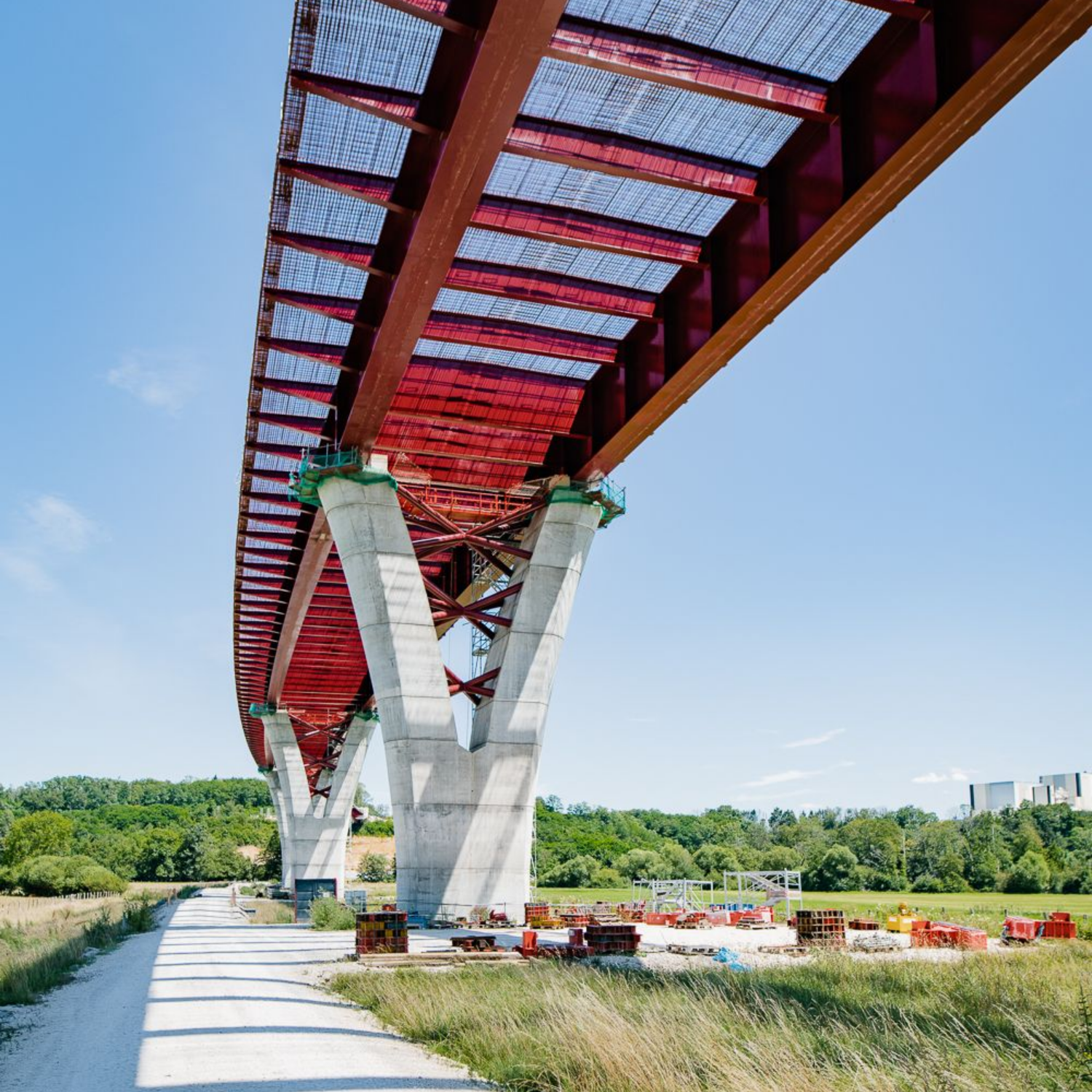 Pont rouge et gris sur un chemin de terre, soutenu par des piliers en béton