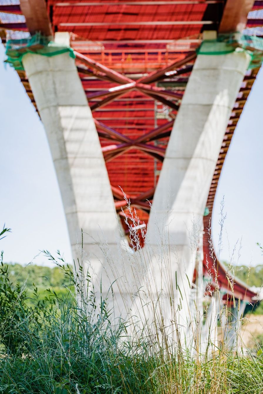 Un pilier de pont en béton, en forme de V, soutenant un pont rouge contre un ciel bleu.