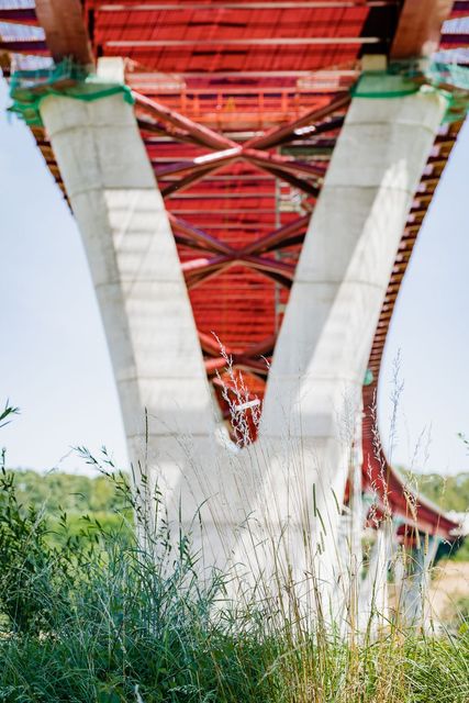 Vue en contre-plongée de la structure de support en béton d'un pont, brun rougeâtre au-dessus, herbe au premier plan