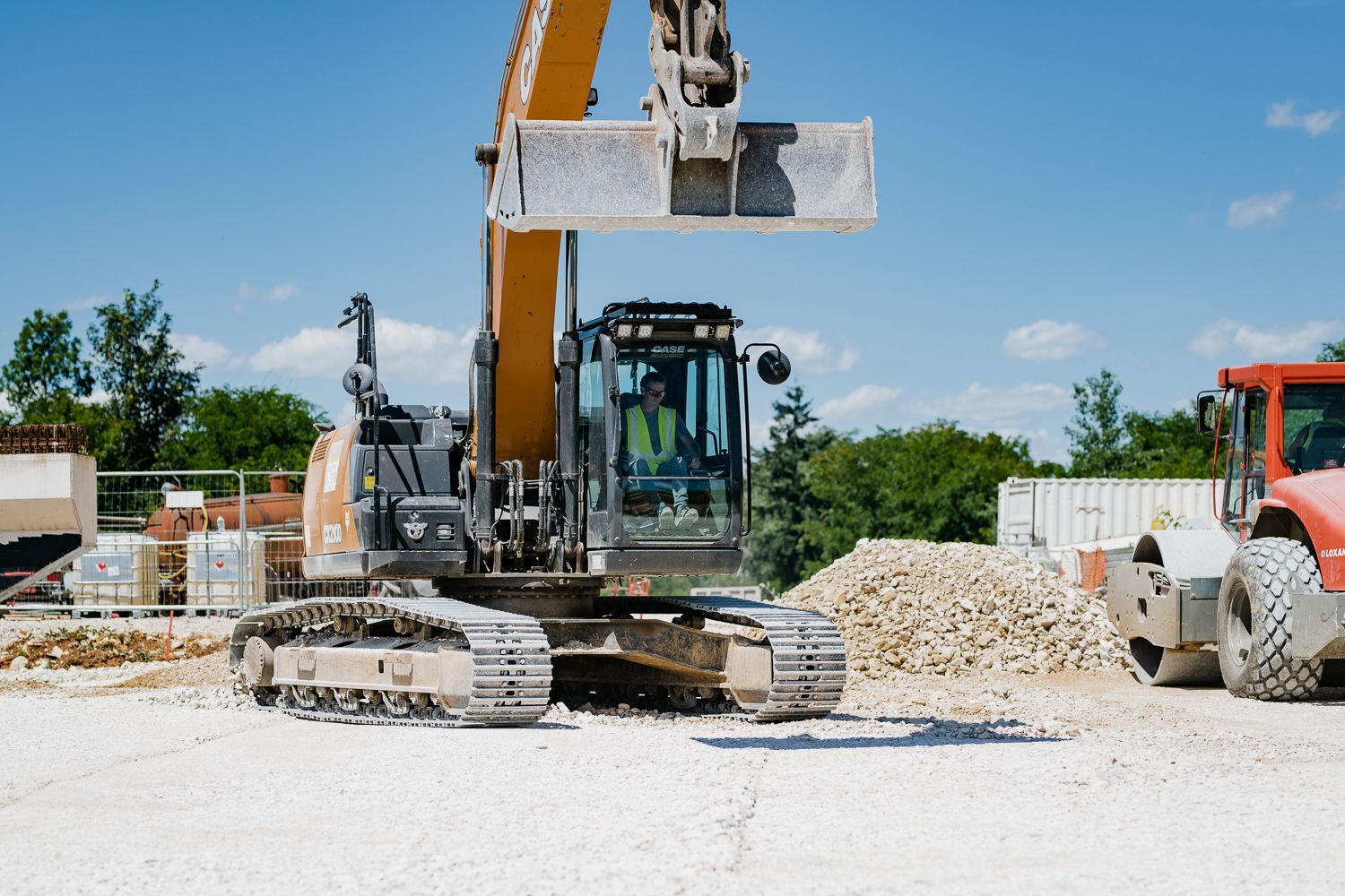 Excavatrice sur un chantier de construction, soulevant son godet rempli de gravats sous un ciel bleu