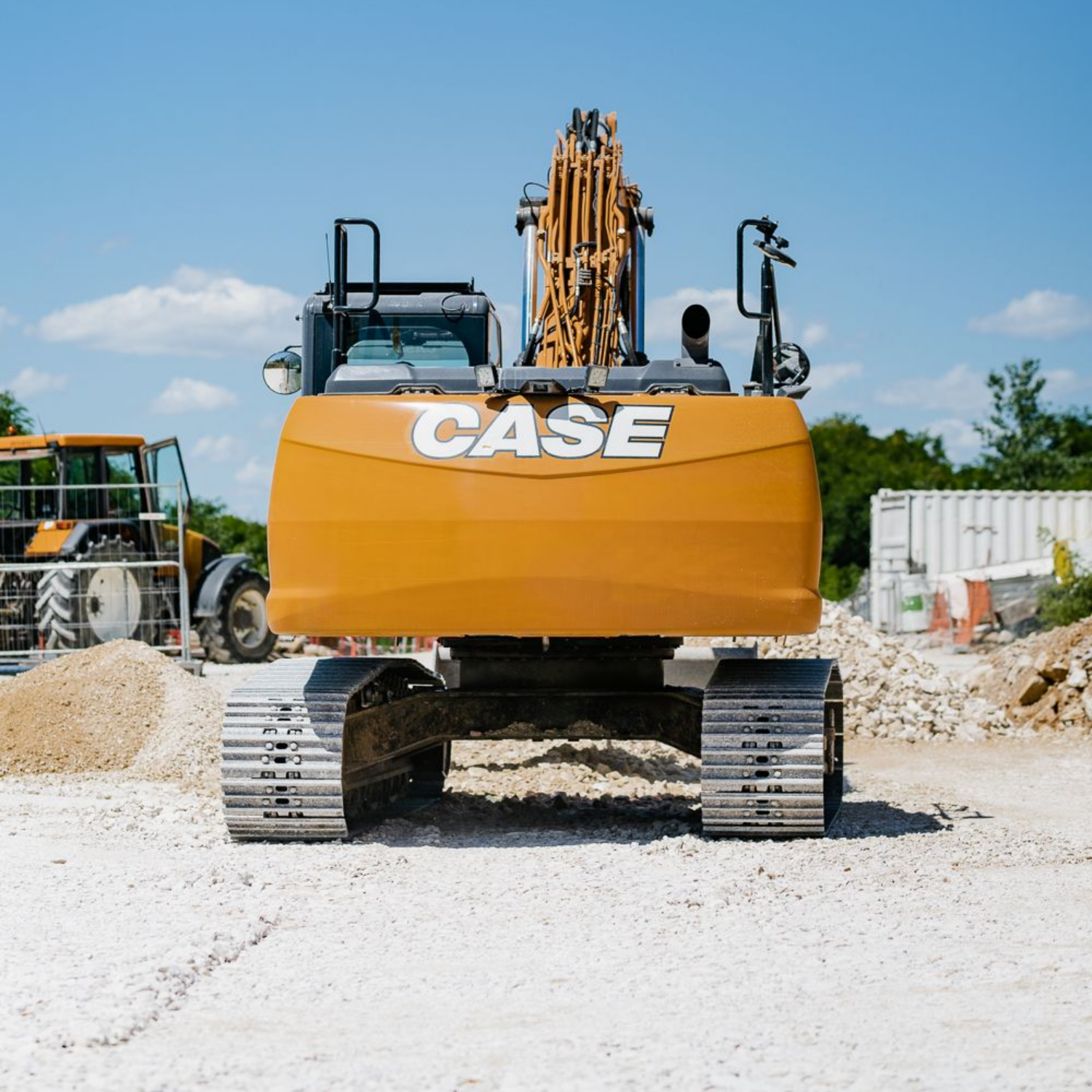 Excavatrice orange Case sur un chantier de construction, avec un tracteur, des débris et un ciel bleu