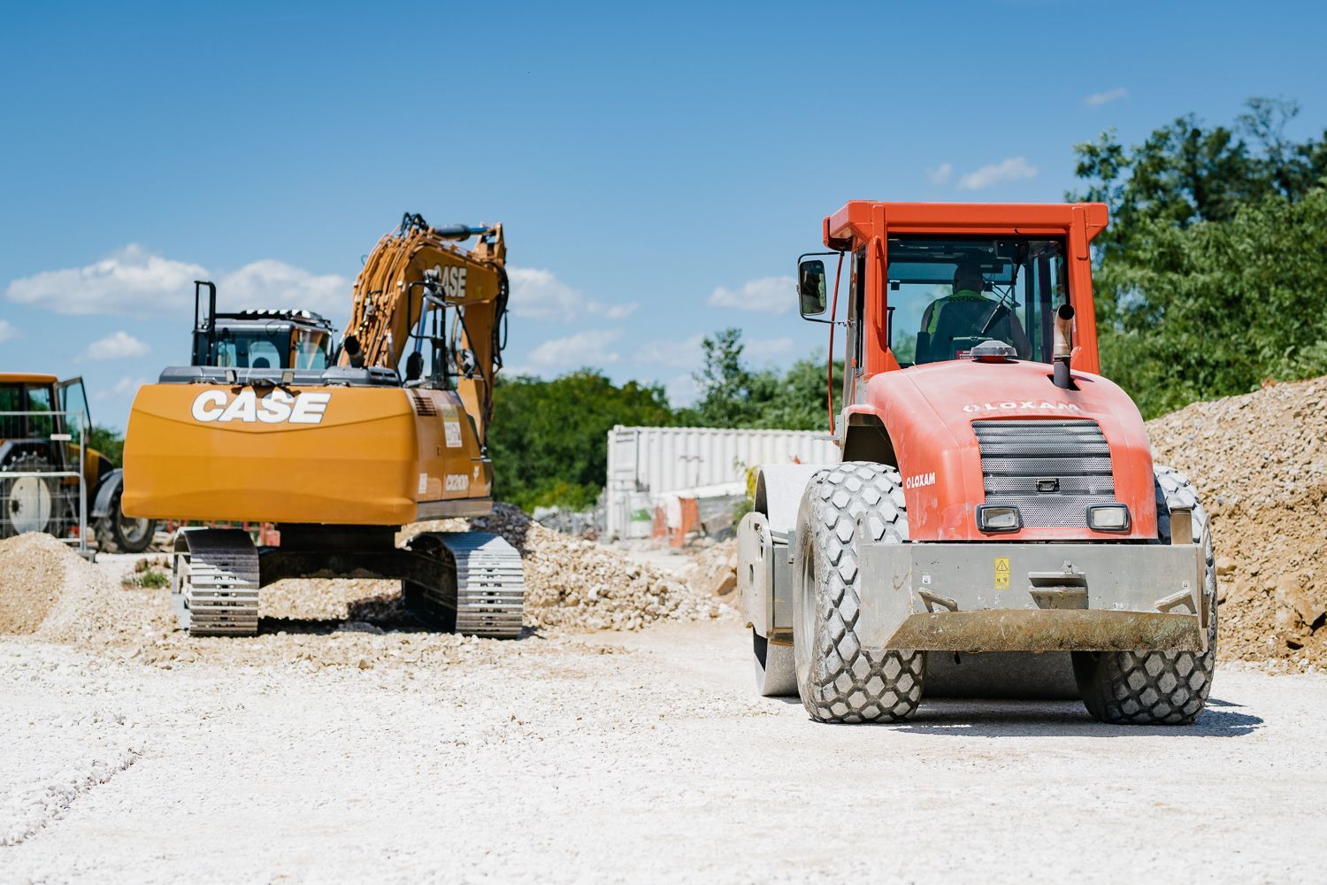 Chantier de construction avec une excavatrice Case orange et un compacteur à rouleau rouge
