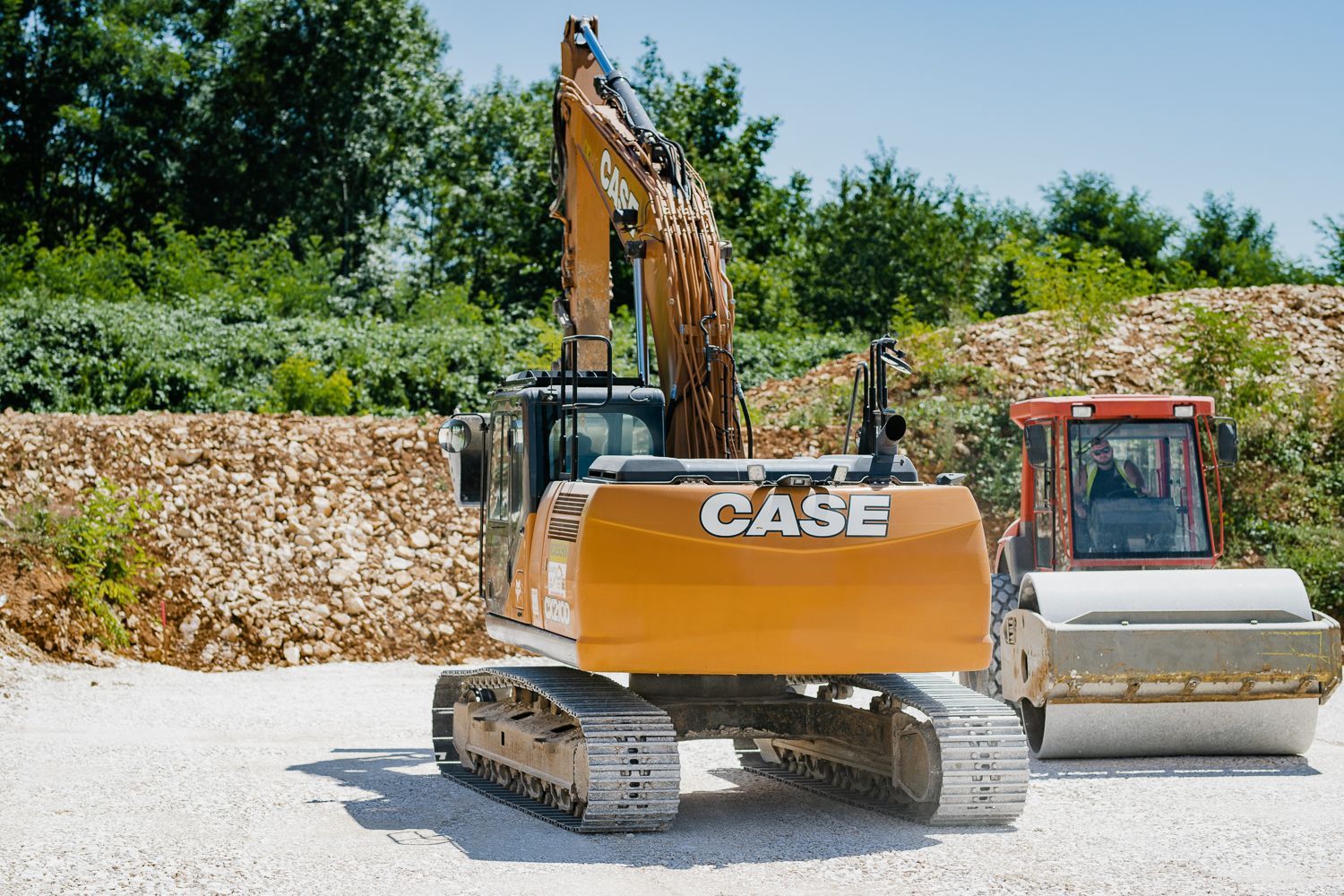 Une excavatrice Case orange et un rouleau compresseur rouge sur un chantier