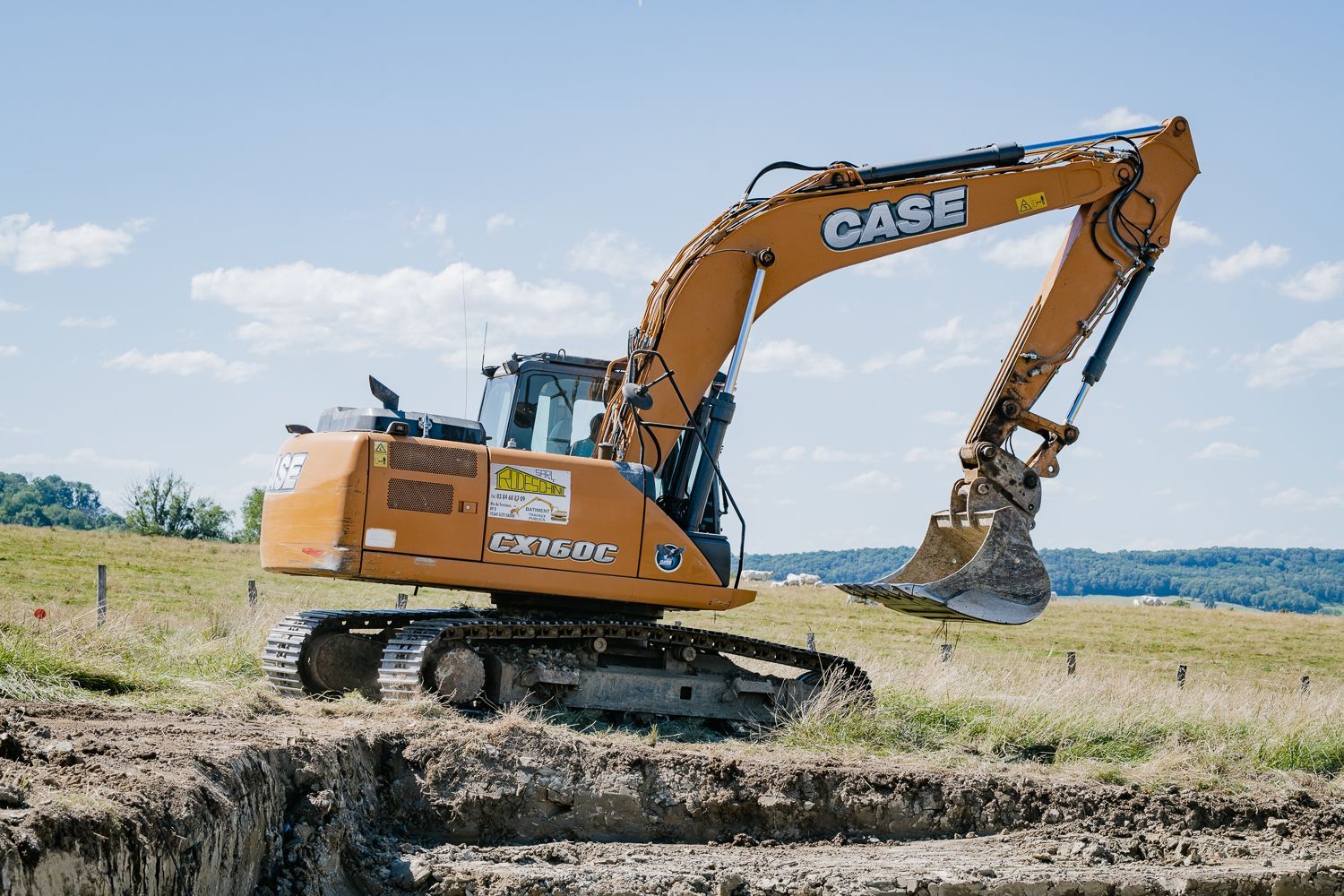 Excavatrice orange Case creusant dans un champ par une journée ensoleillée
