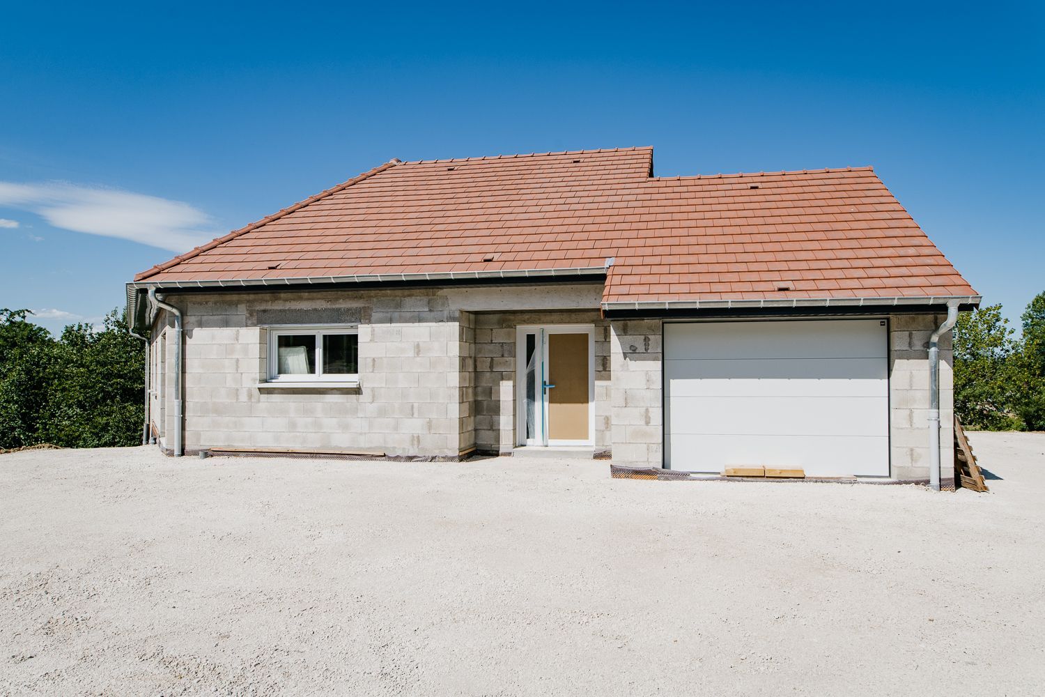 Maison neuve en construction avec murs en parpaings, toit en tuiles rouges et allée en gravier