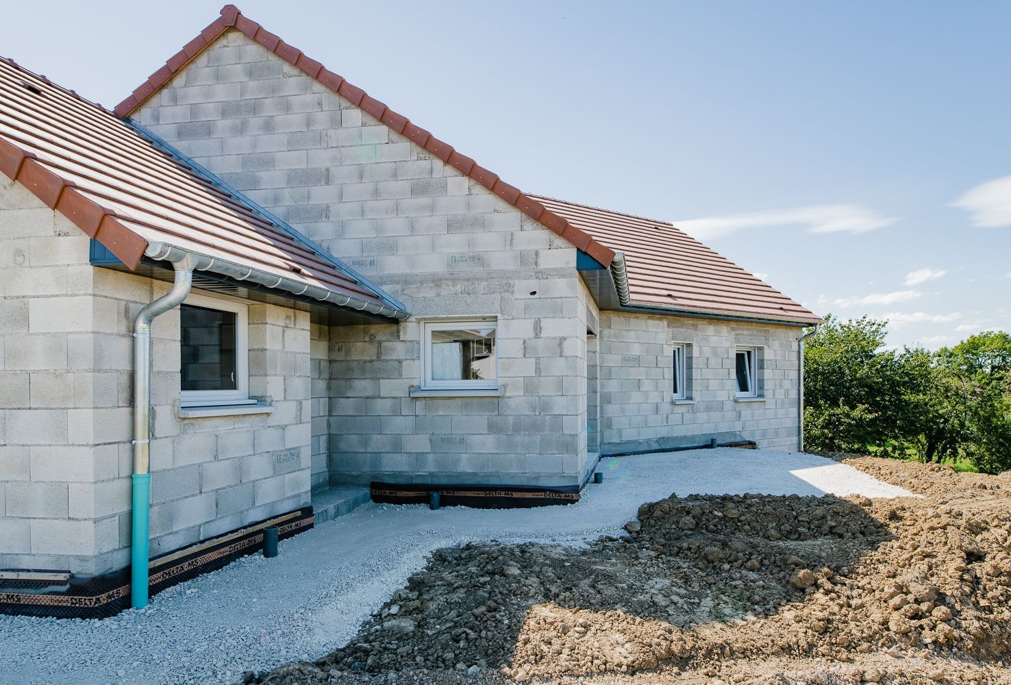 Maison neuve en construction, parpaings gris, toiture rouge, allée de gravier