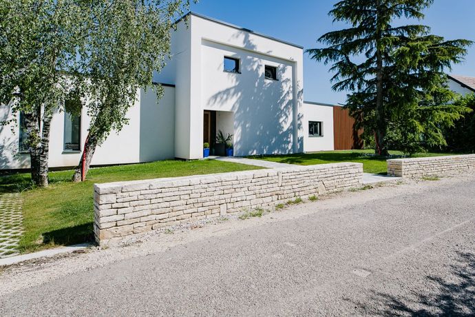 Maison blanche moderne avec murs de soutènement en pierre, pelouse verte et allée en gravier
