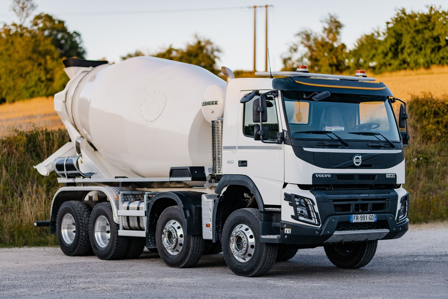 Camion malaxeur à béton blanc sur une route ; arrière-plan de campagne avec des arbres