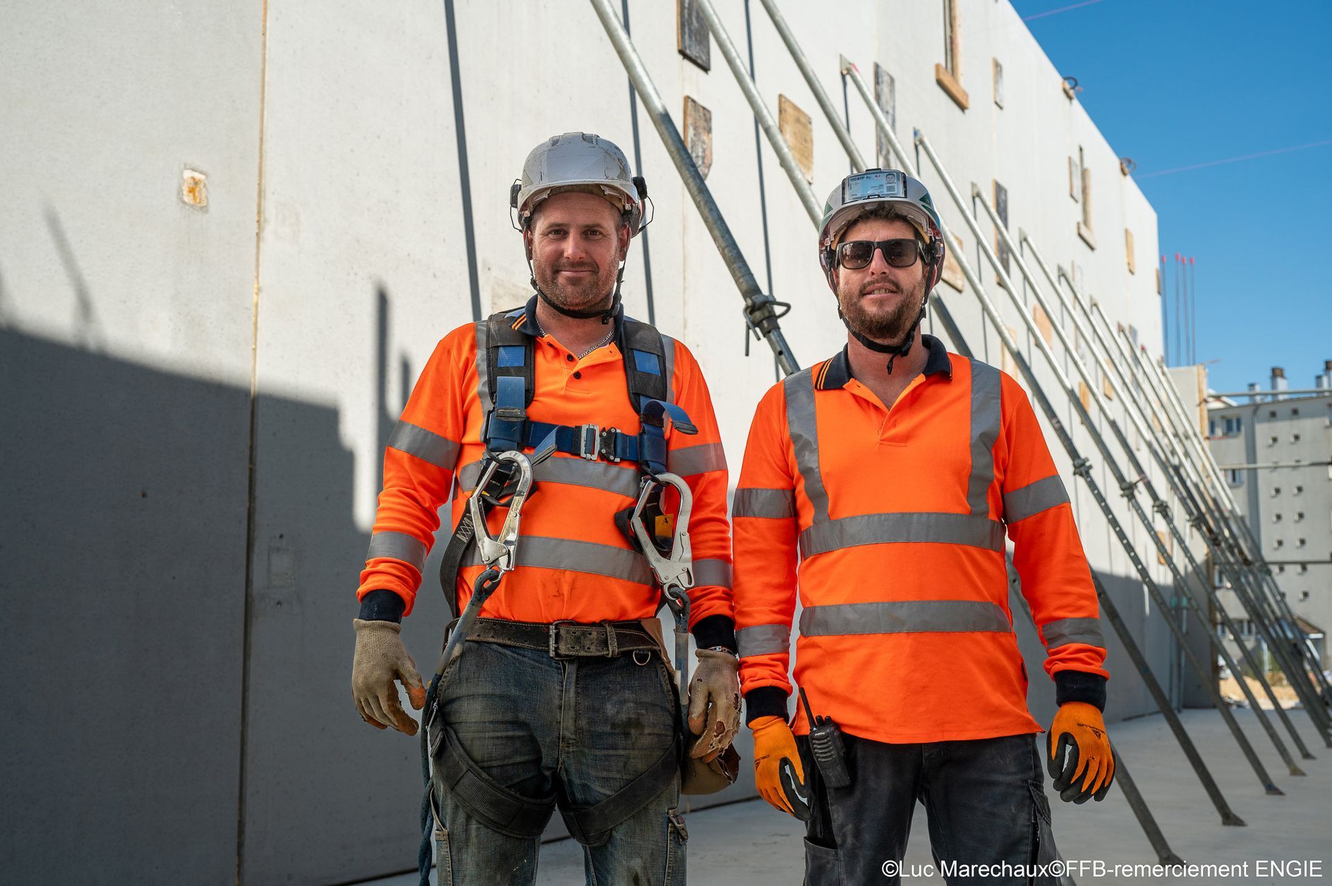 Deux ouvriers du bâtiment en tenue de sécurité posent devant un bâtiment