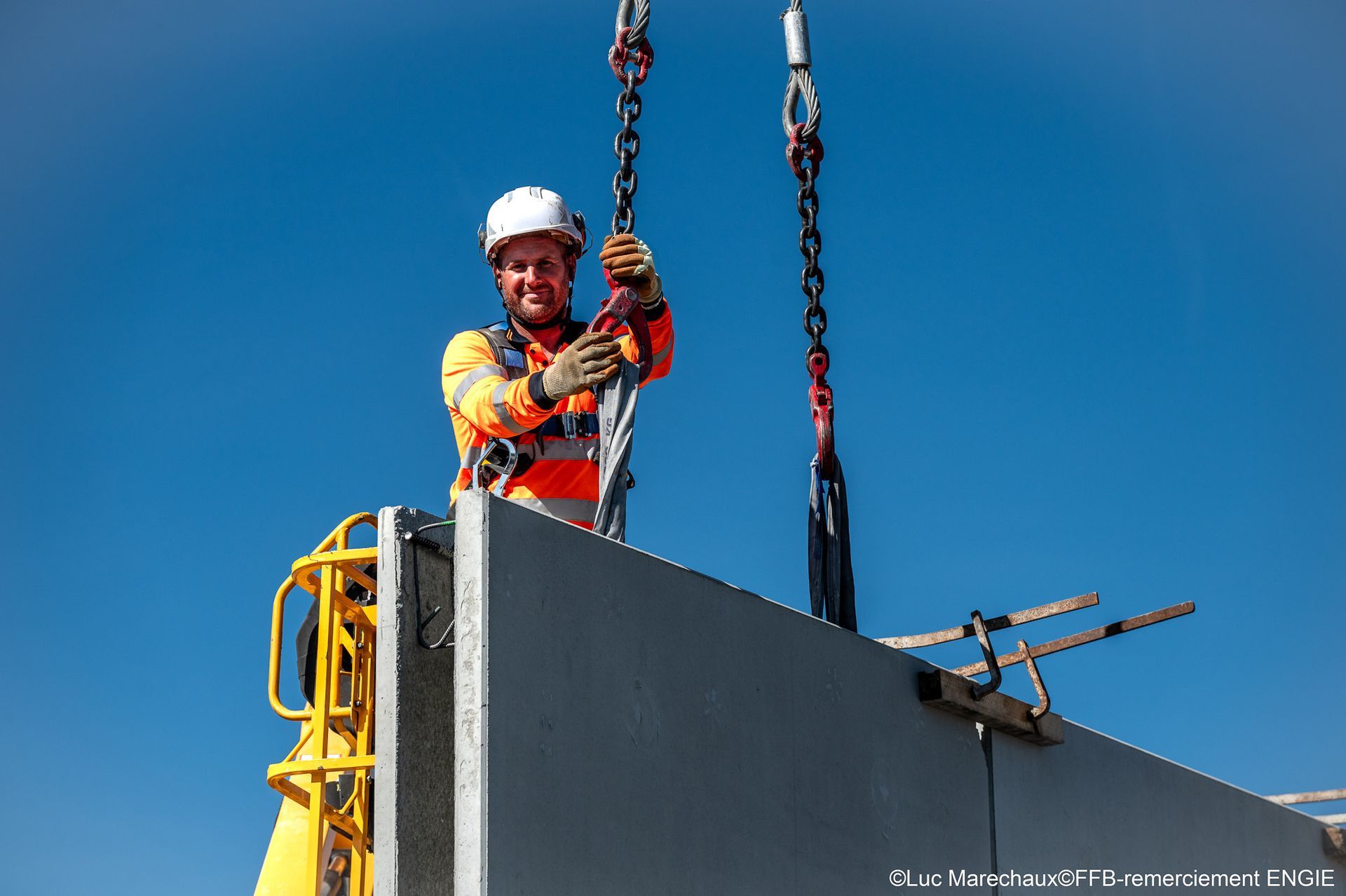 Ouvrier du bâtiment en tenue de sécurité guidant un panneau suspendu par des chaînes