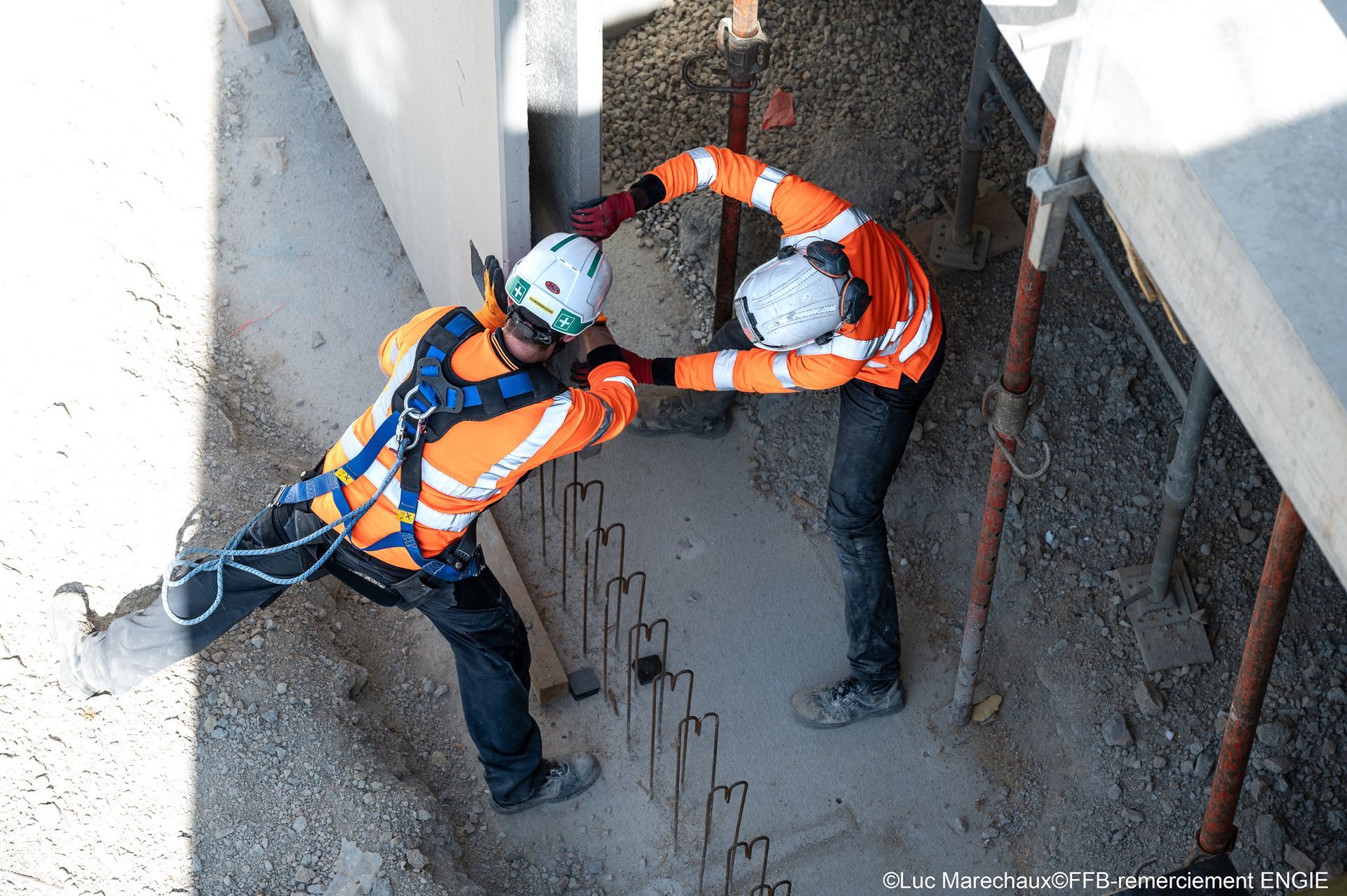 Deux ouvriers du bâtiment portant des gilets et des casques orange travaillent dans une tranchée