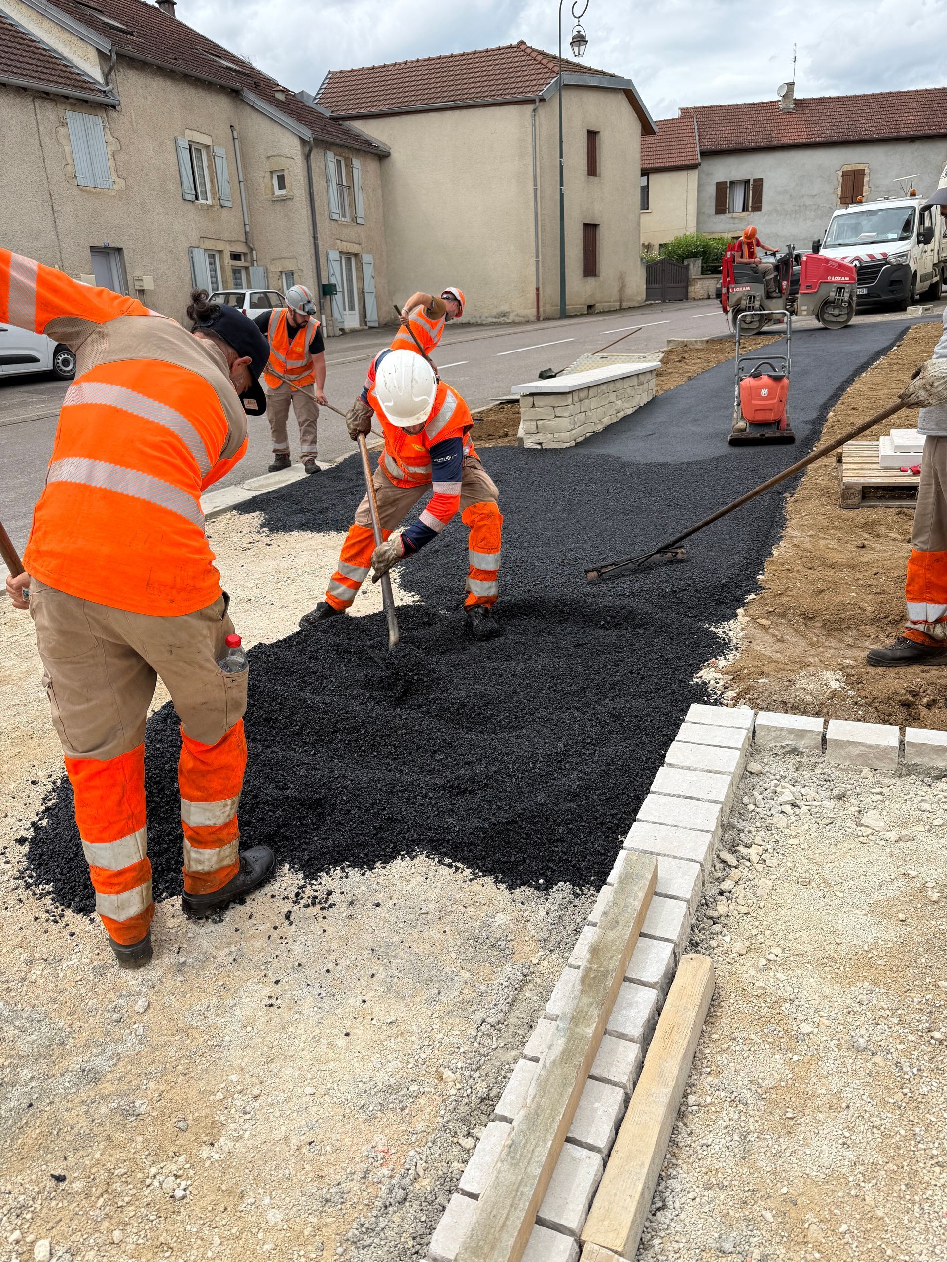 Des ouvriers du bâtiment portant des gilets orange posent de l'asphalte sur une route sur une place de la ville
