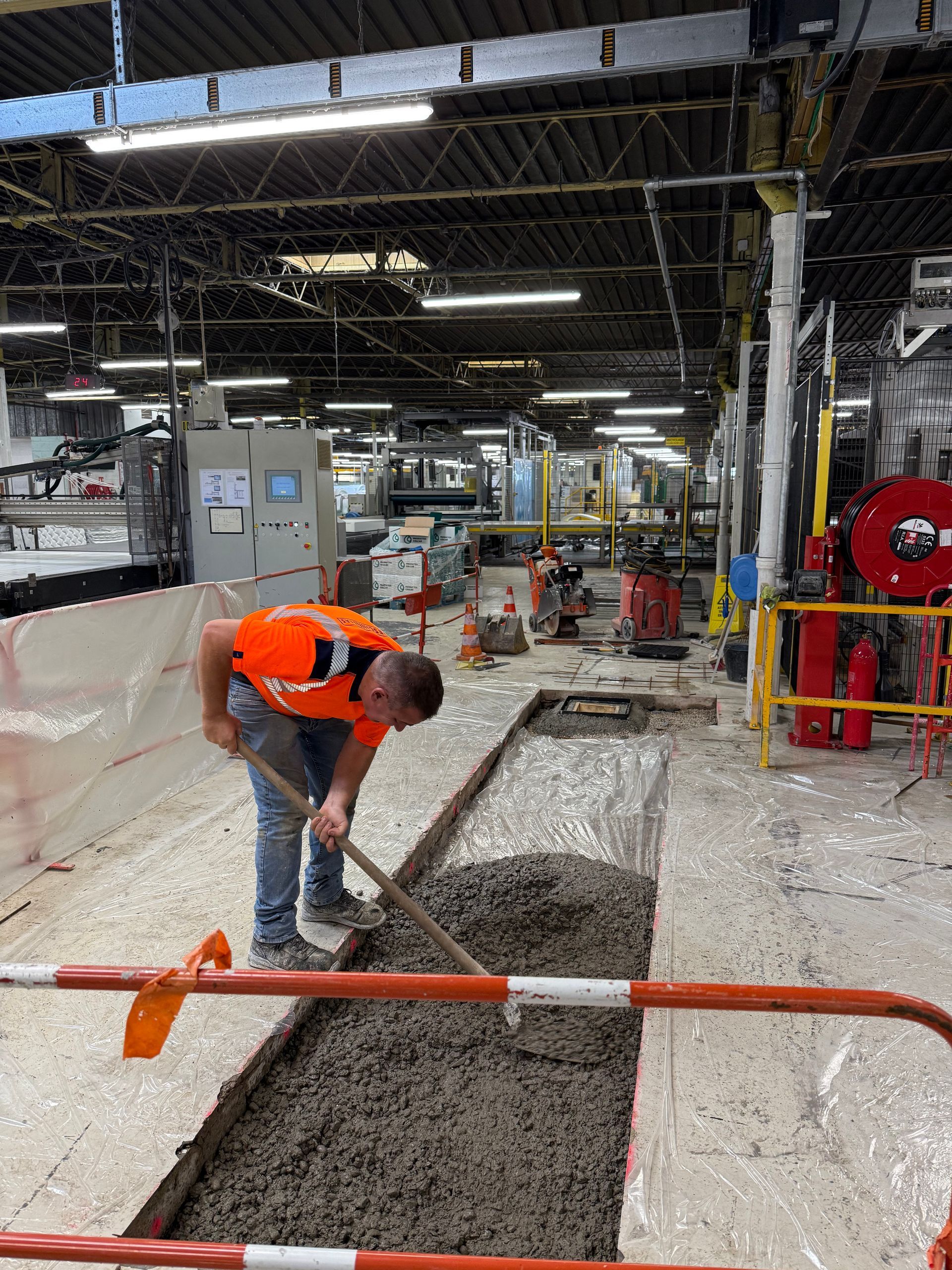 Un homme en gilet orange pelletant du béton dans un bâtiment industriel