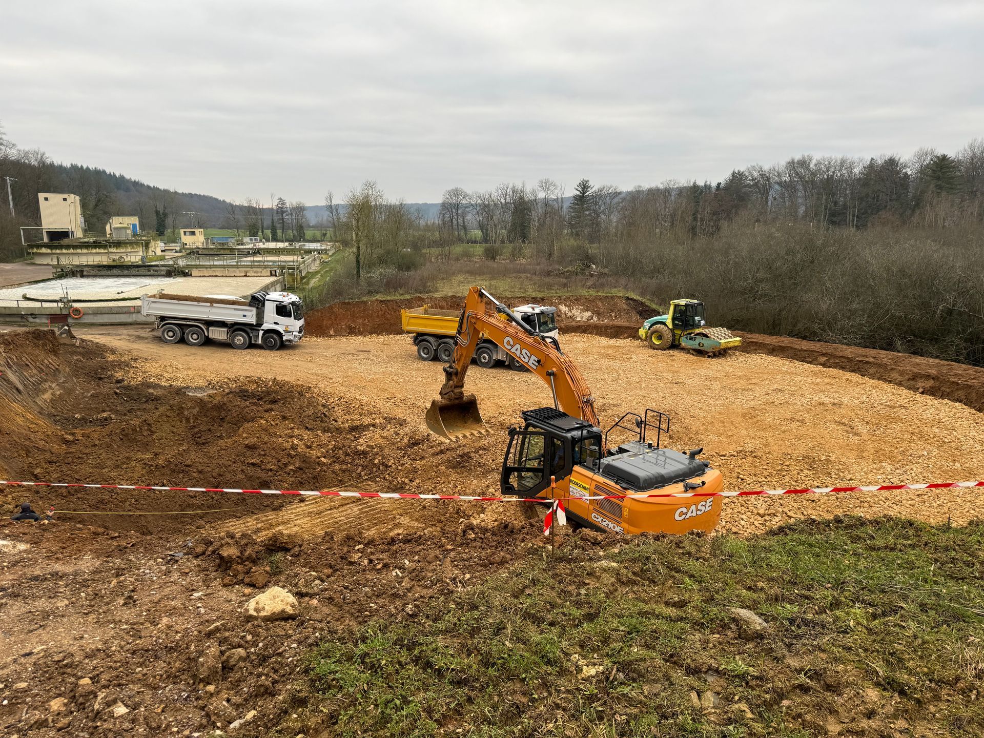 Chantier de construction avec une excavatrice, des camions et un rouleau compresseur