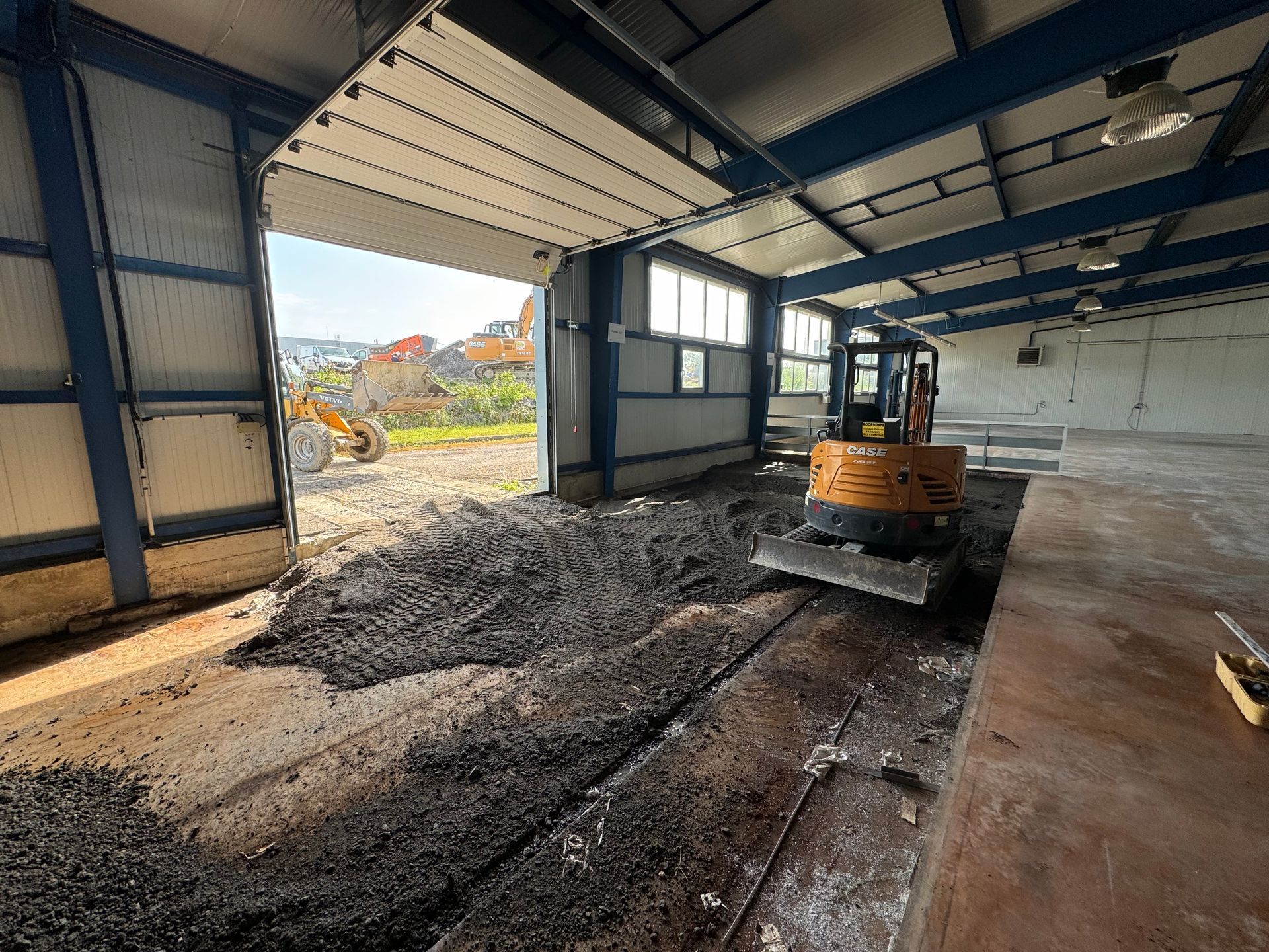 Excavatrice à l'intérieur d'un entrepôt ouvert ; enlèvement de débris, poutres bleues, murs gris