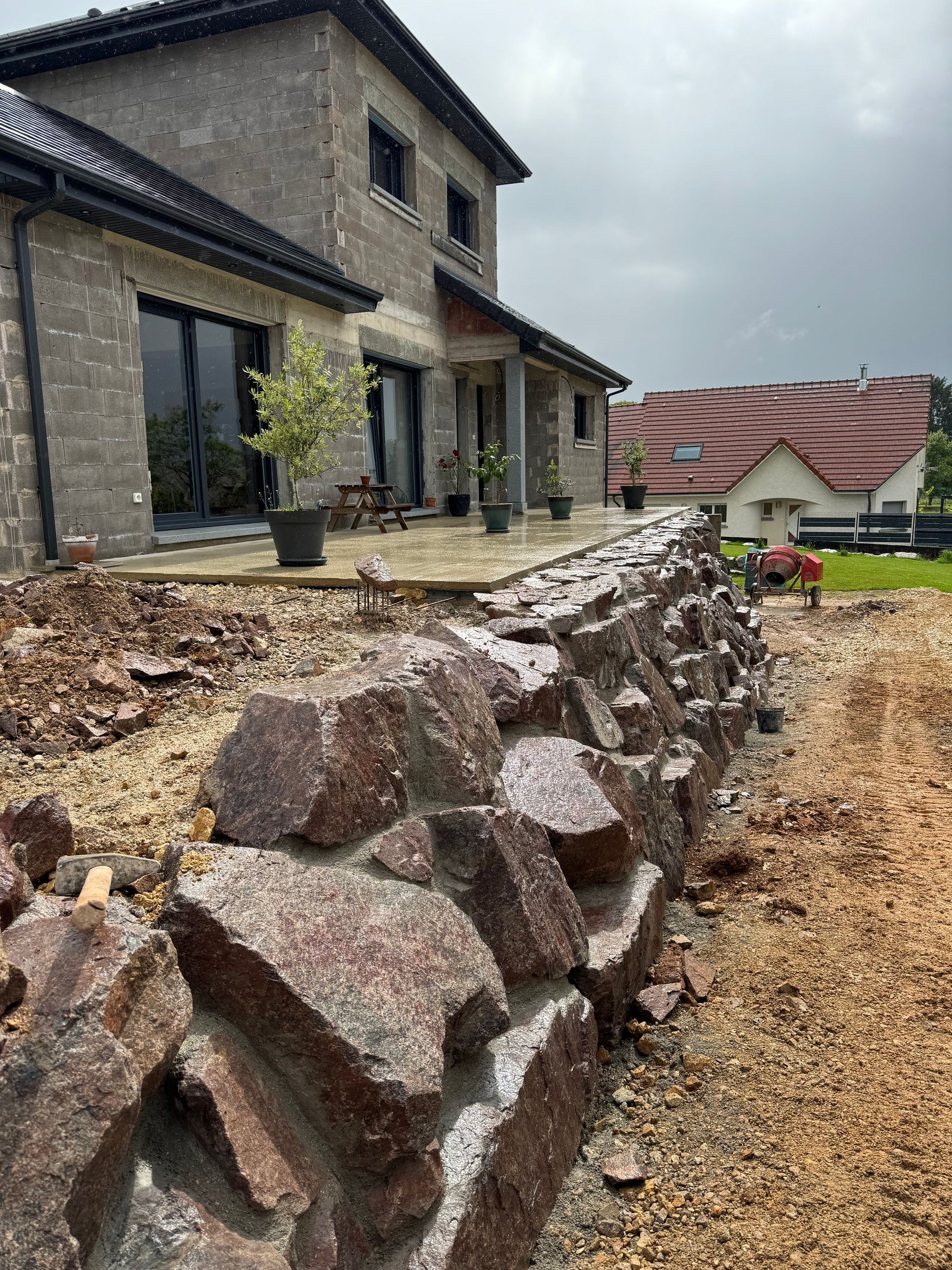 Mur de soutènement en granit devant une maison avec de grandes fenêtres, sous un ciel nuageux