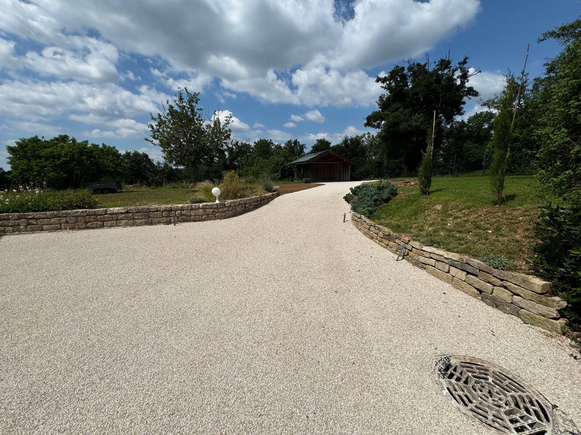 Une allée de gravier serpente vers un bâtiment en bois dans un paysage verdoyant