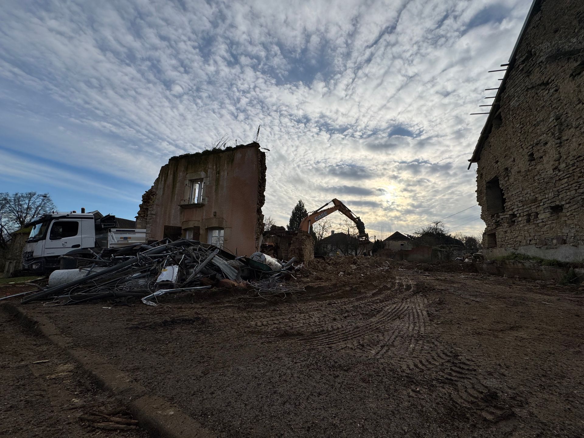 Démolition de bâtiments sous un ciel nuageux avec une excavatrice et des débris
