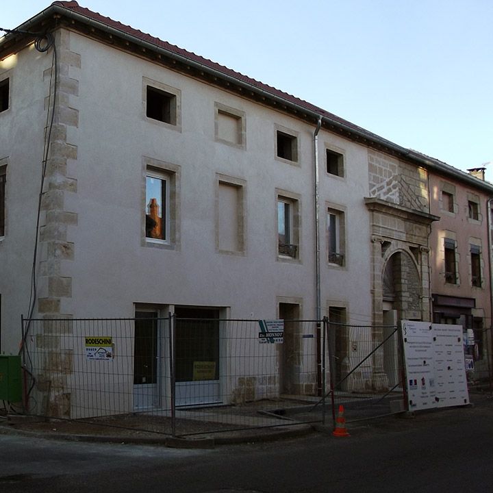 Bâtiment en rénovation avec façade en pierre calcaire, fenêtres manquantes et clôture de chantier
