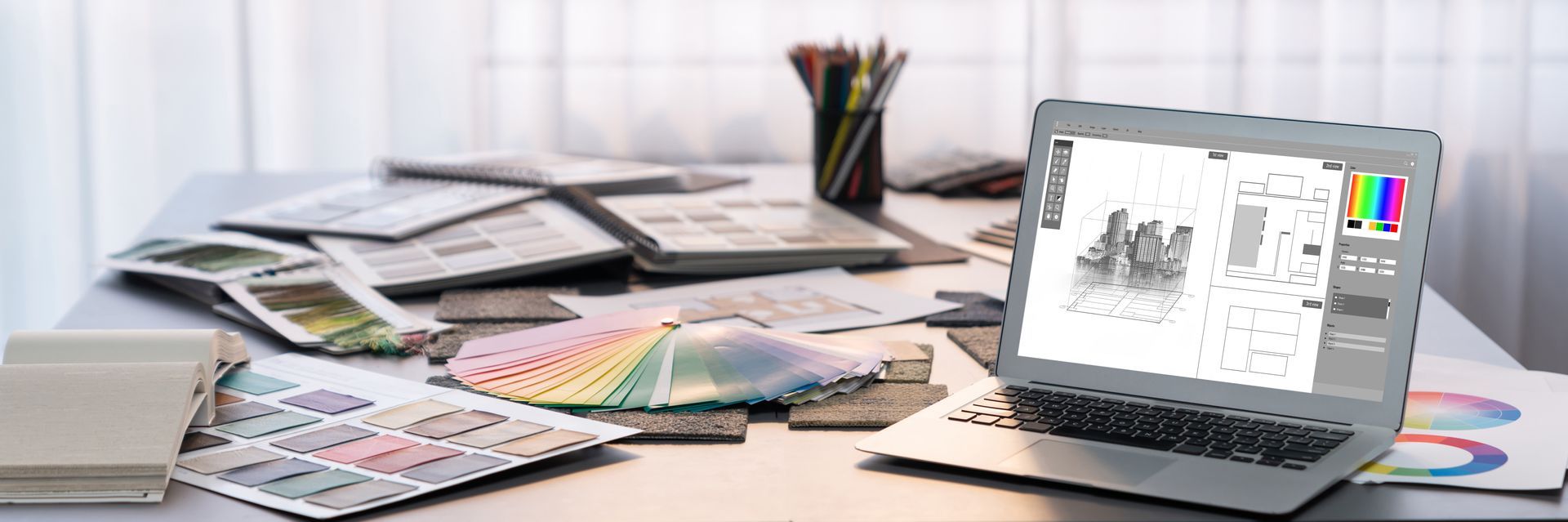 Espace de travail d'un designer avec ordinateur portable, nuanciers, croquis et papiers éparpillés sur un bureau