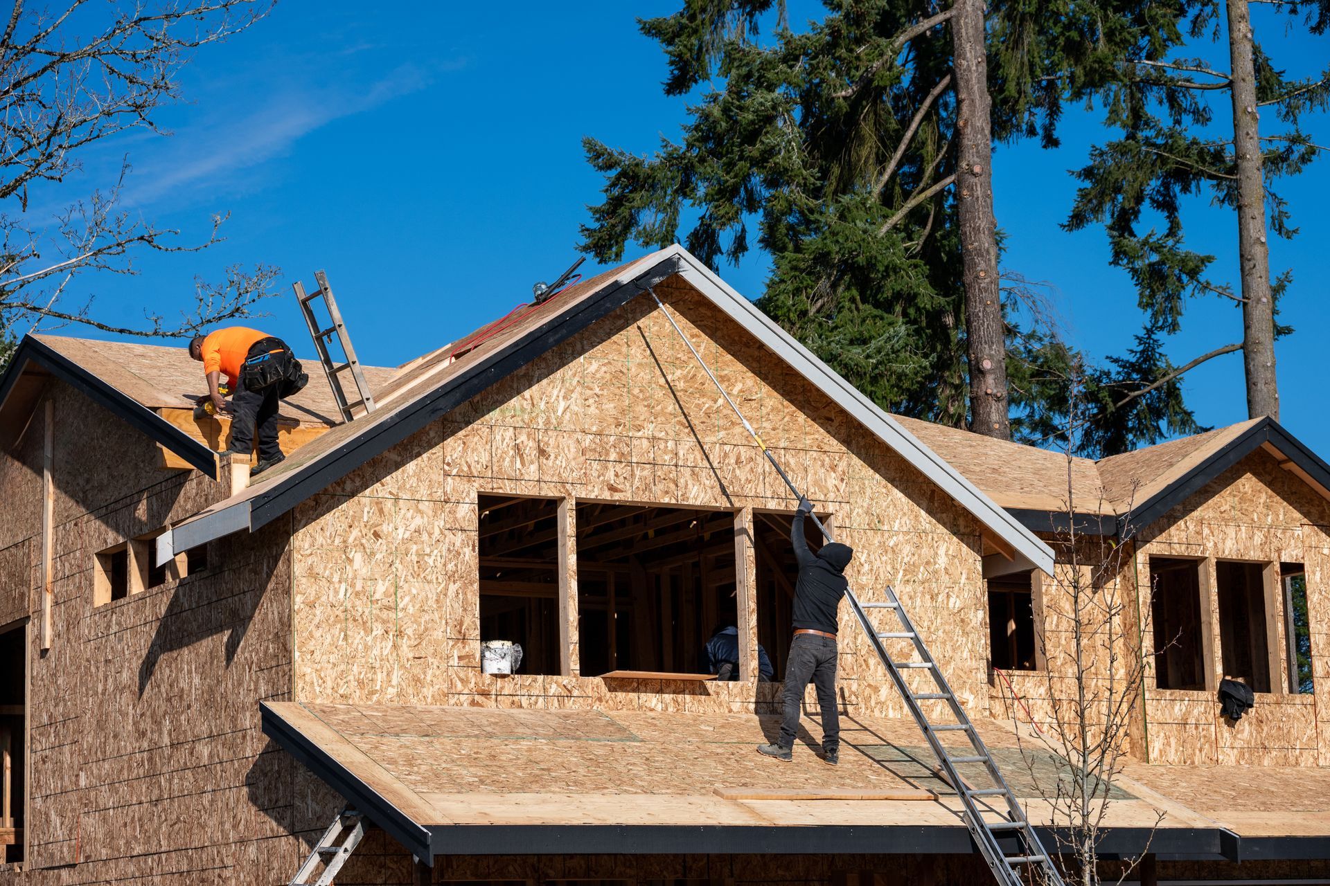 Des couvreurs posent des bardeaux sur une maison en construction, sur fond de ciel bleu.