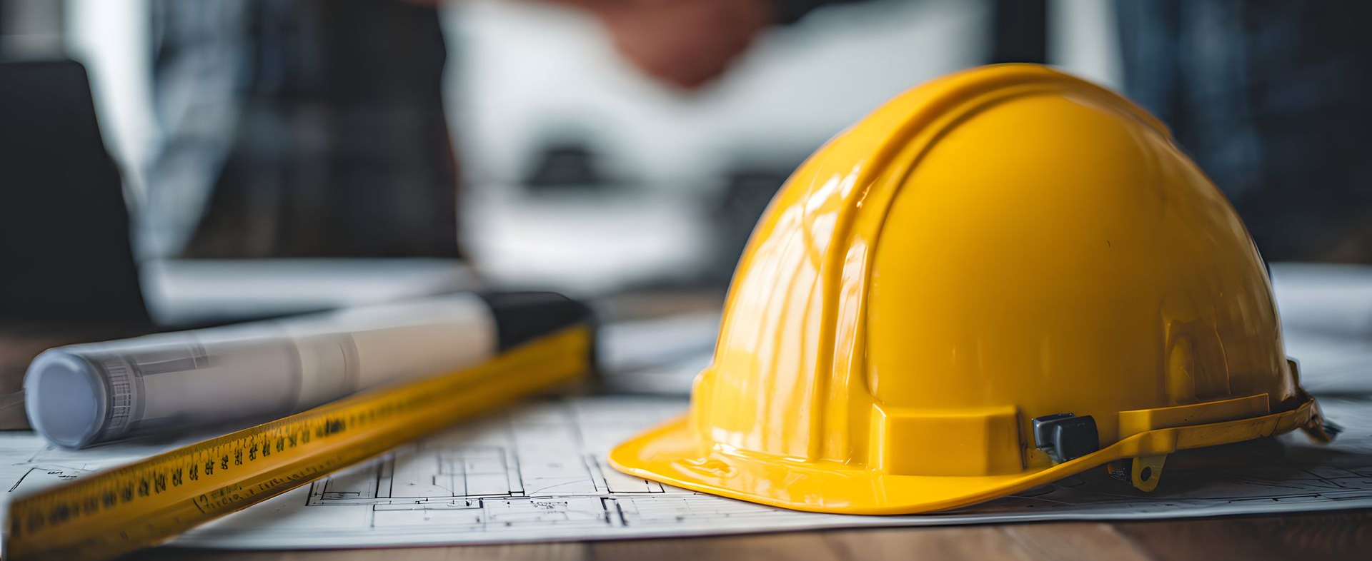 Casque de chantier jaune sur des plans de construction avec un crayon et un plan enroulé.