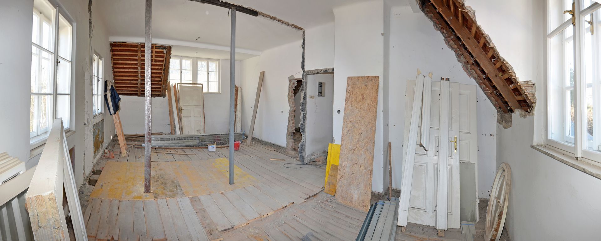 Grenier partiellement rénové avec poutres apparentes, échelles et matériaux de construction près d'une fenêtre de toit