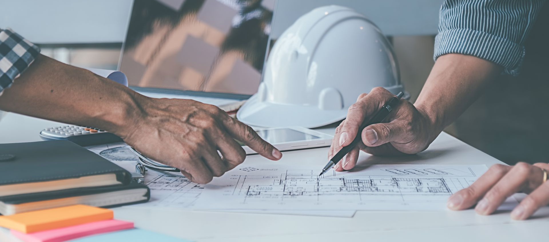 Des personnes examinent des plans d'architecte et des schémas architecturaux autour d'une table de conférence, pointant du doigt et prenant des notes.