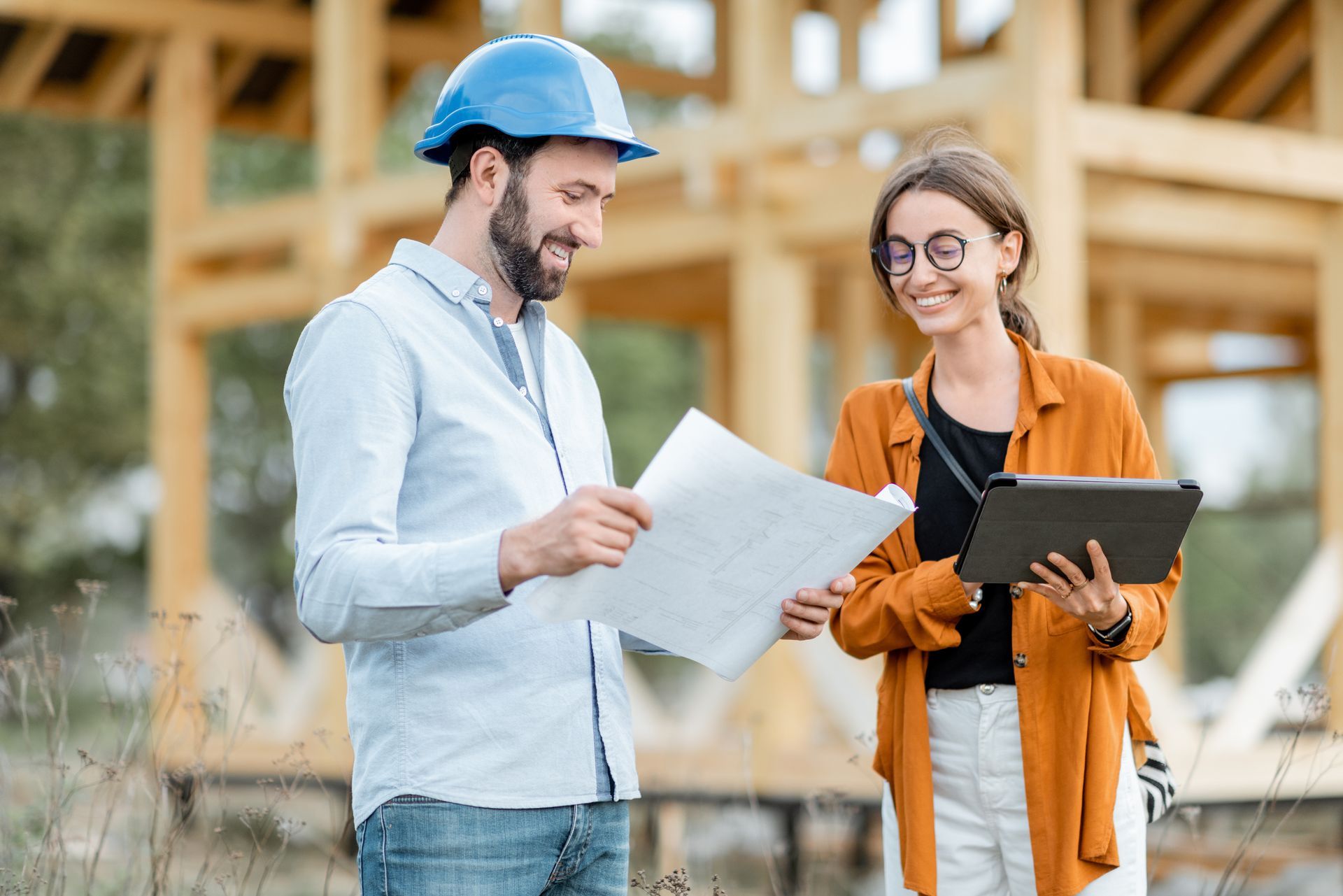 Deux ouvriers du bâtiment examinent des plans sur un chantier, l'un tenant une tablette et l'autre portant un casque de chantier bleu.