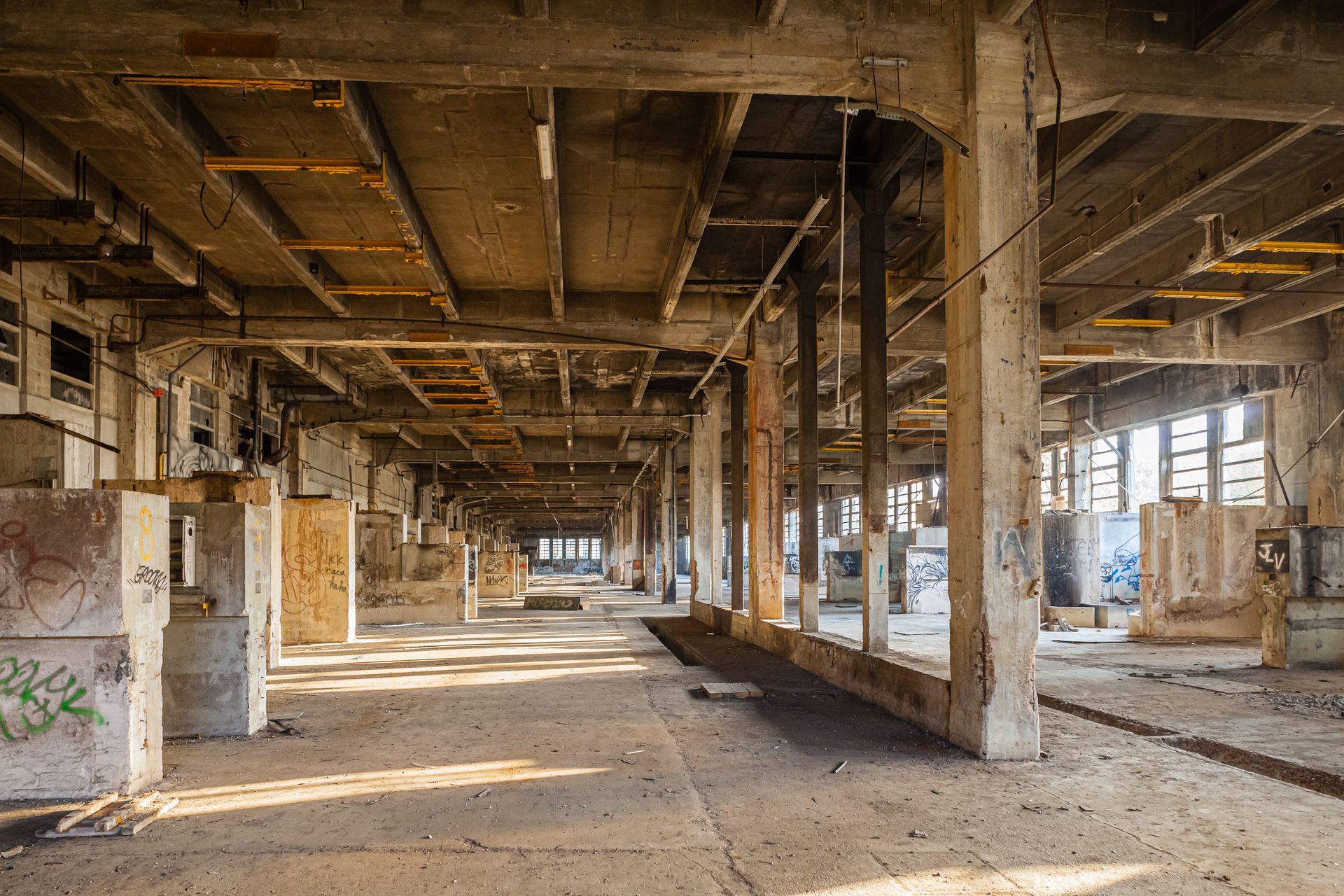 Intérieur d'un entrepôt industriel abandonné avec des piliers en béton, des poutres apparentes et des débris au sol