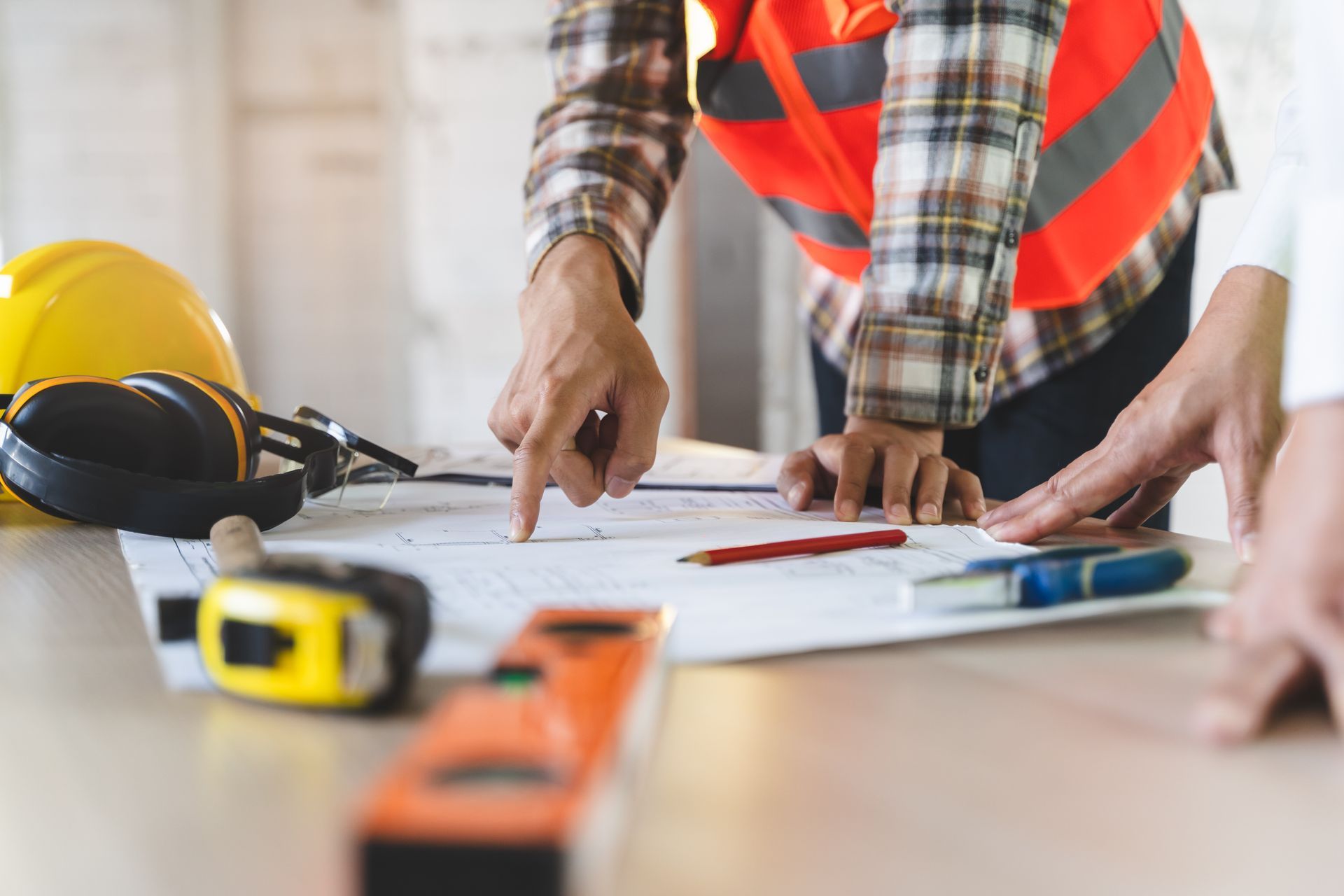 Des ouvriers du bâtiment, casques, gilets de sécurité et outils en main, examinent des plans à une table.