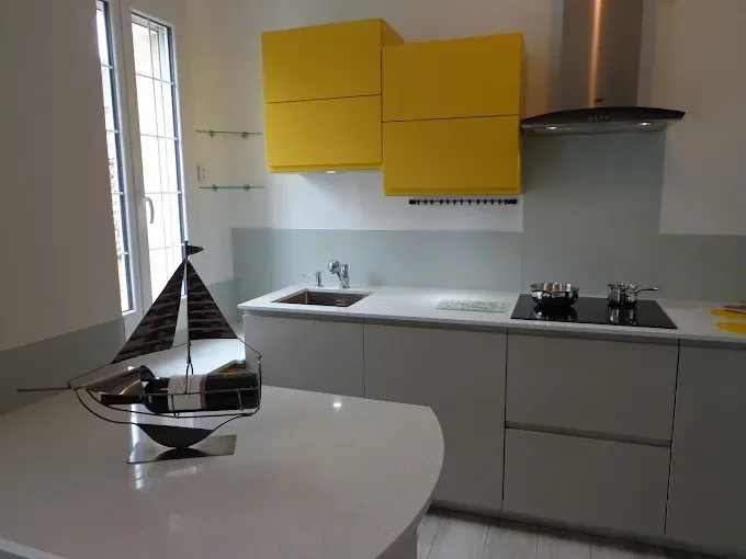 Cuisine moderne avec placards en bois clair, plan de travail foncé et table avec chaises.