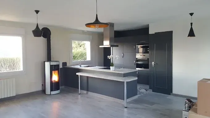 Cuisine avec mur rouge, plan de travail gris, appareils électroménagers noirs et deux tabourets de bar noirs.