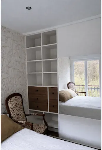 Meuble encastré blanc placé à côté d'une fenêtre, avec bureau coulissant, étagères et tiroirs.