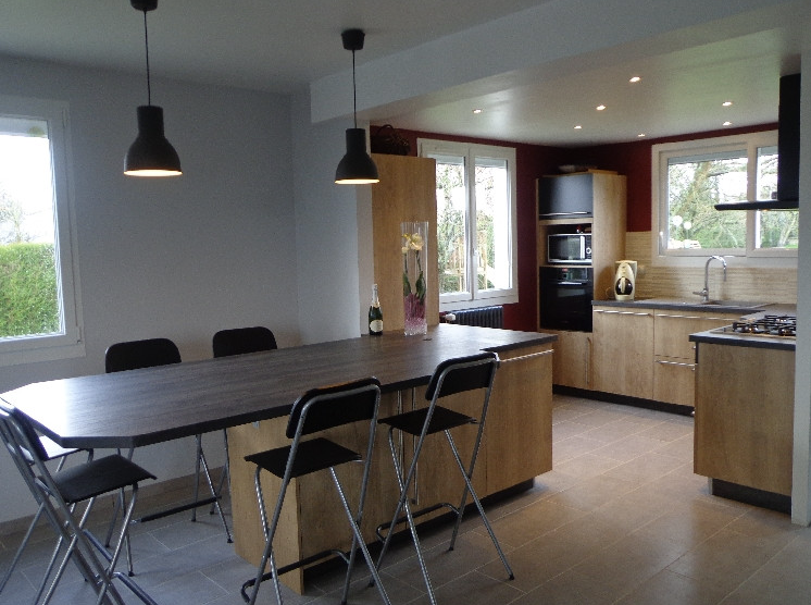 Cuisine moderne avec armoires grises, électroménagers en acier inoxydable, îlot central et sol carrelé.