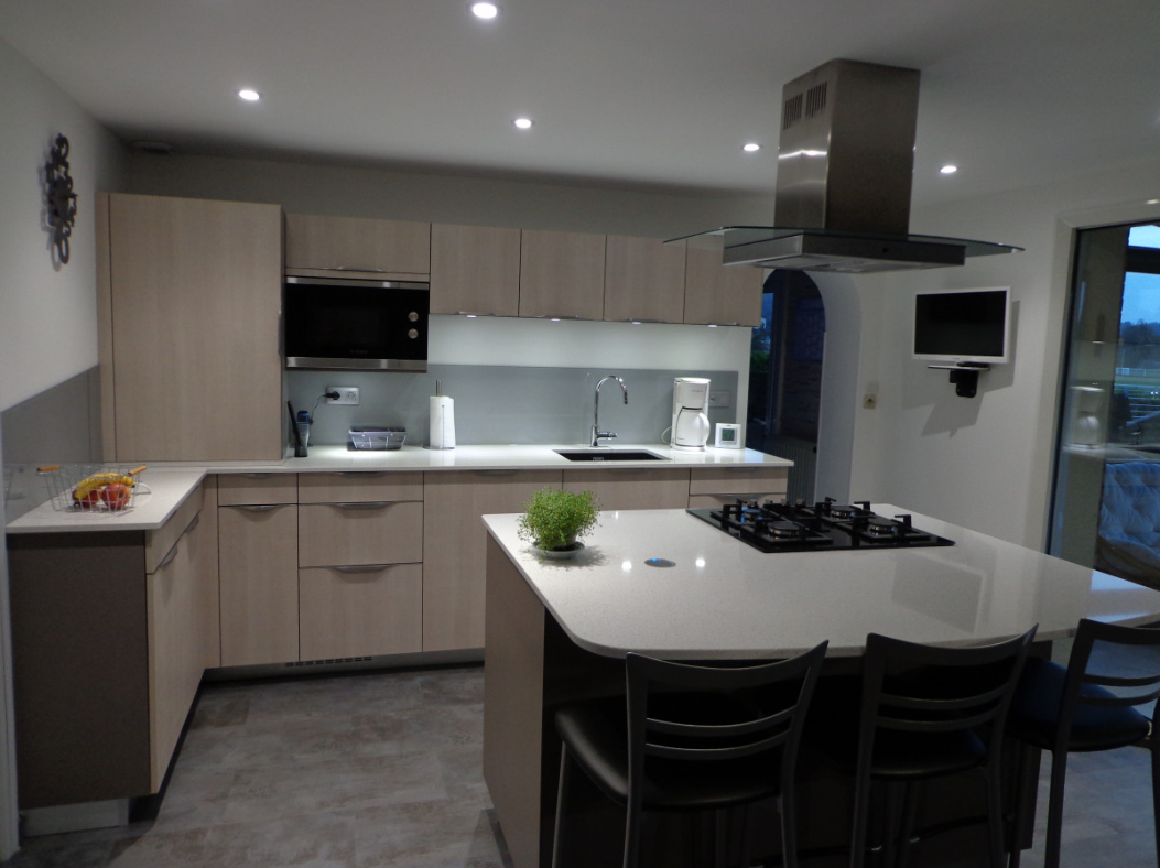 Cuisine moderne avec armoires en bois clair, appareils électroménagers en acier inoxydable et îlot central avec sièges.