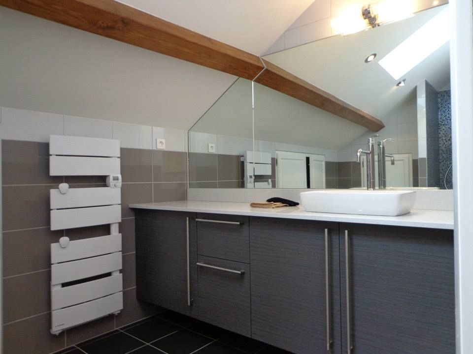 Salle de bains moderne avec meubles gris, lavabo blanc et sèche-serviettes blanc ; le miroir reflète la lumière.