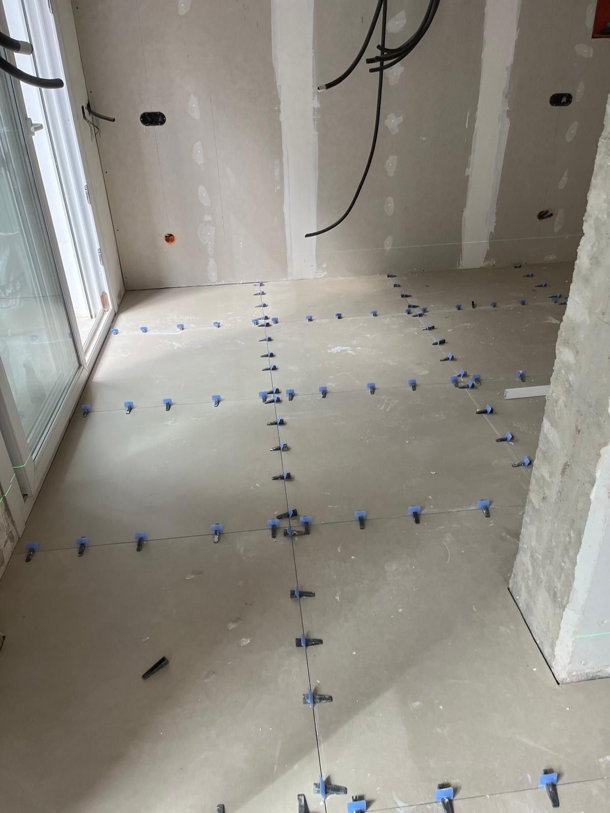 Habitación sin terminar con suelo blanco delimitado con cinta azul y paredes sin pintar cerca de una puerta corredera de cristal.