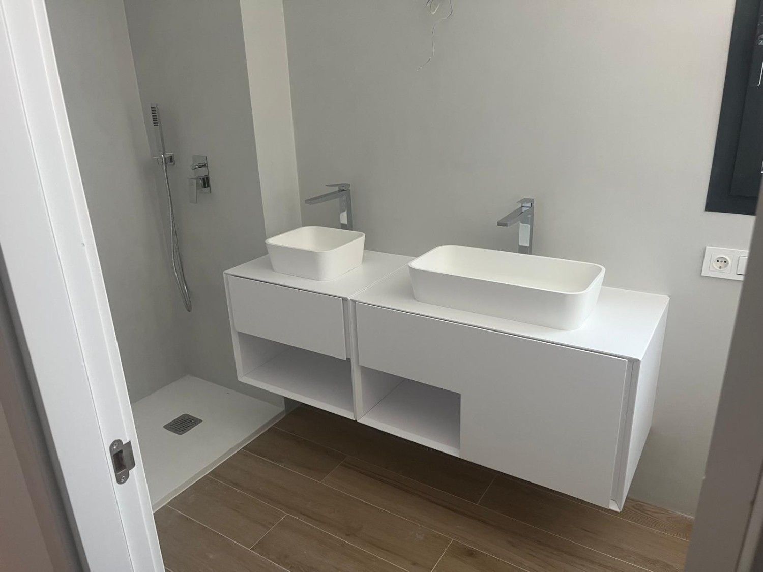 Baño moderno con tocador doble blanco, lavabos cuadrados, paredes grises y baldosas de suelo con aspecto de madera.