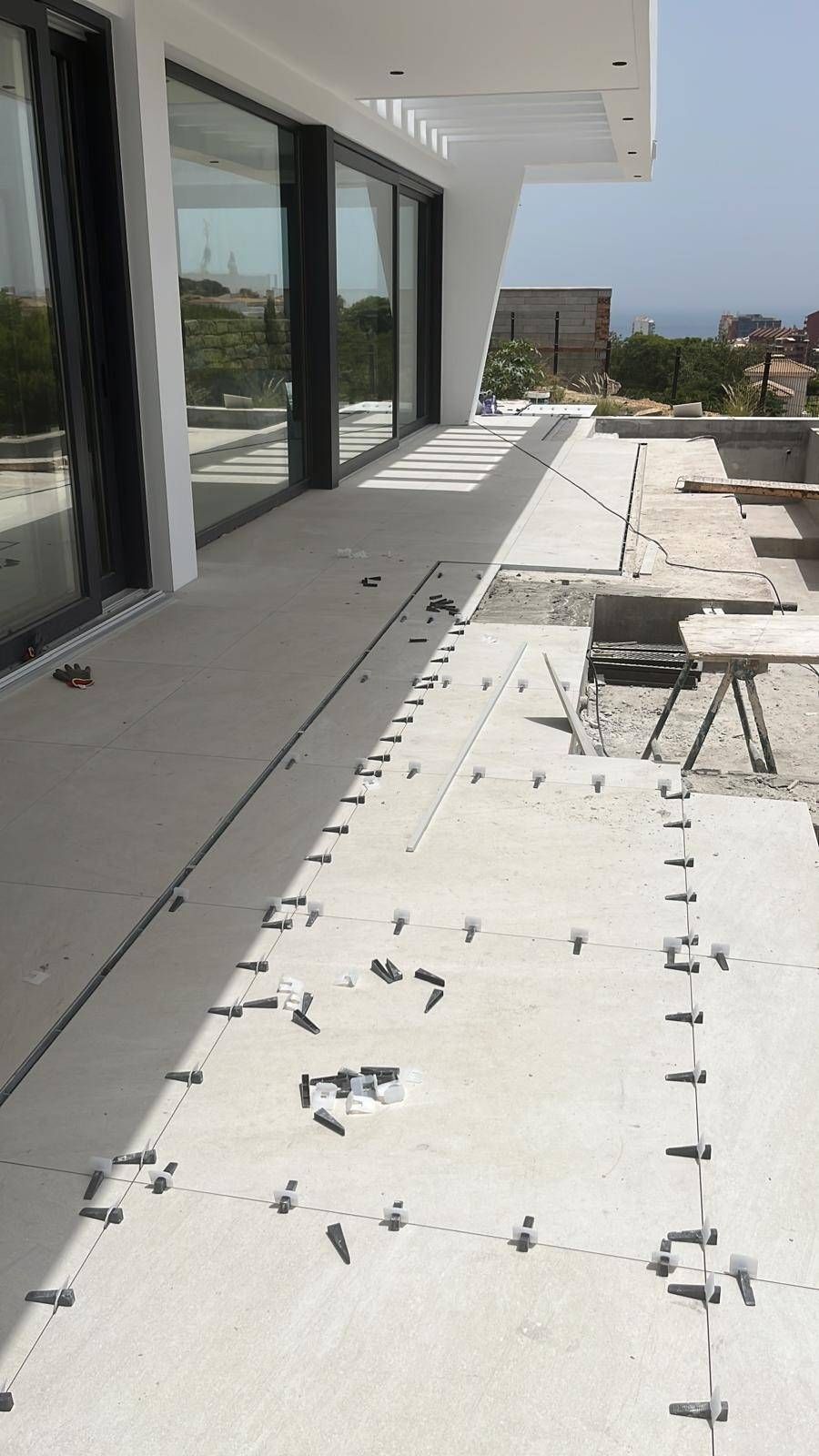 Terraza en la azotea con suelo blanco, escombros dispersos y grandes puertas de cristal junto a un edificio moderno.