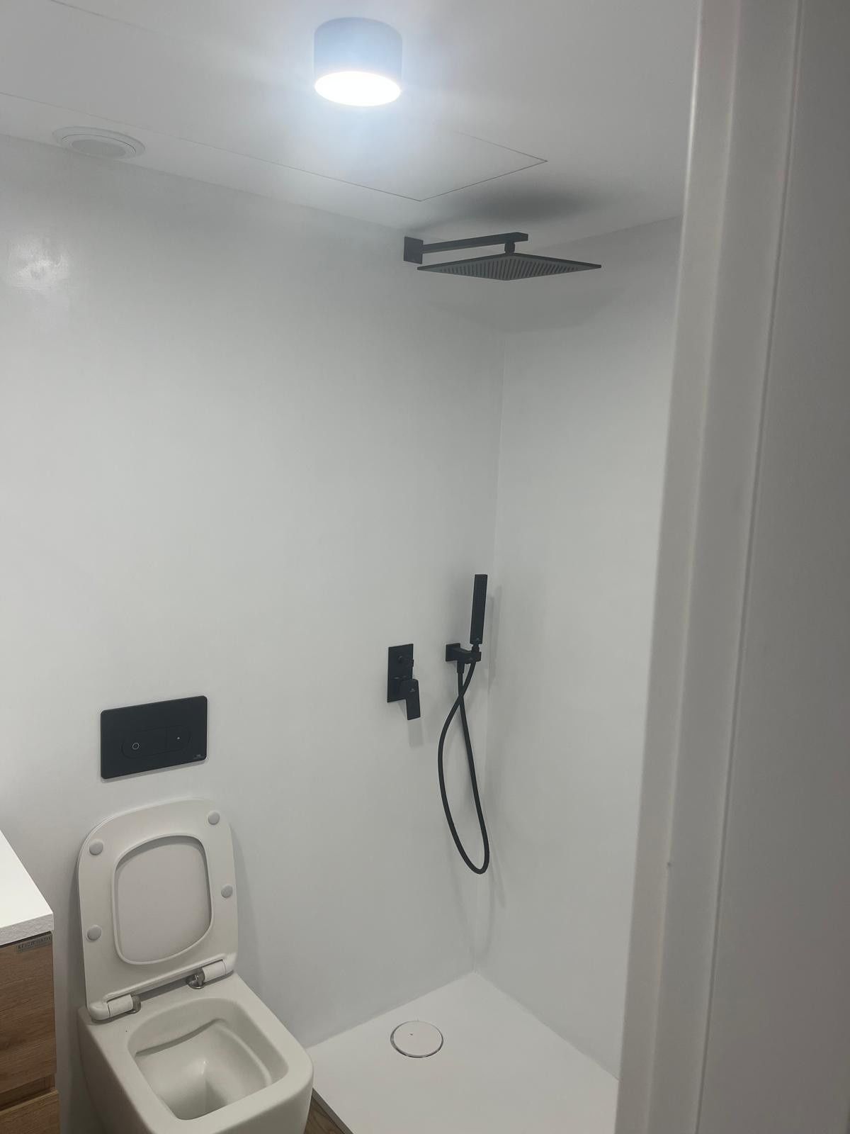 Baño pequeño de color blanco con inodoro abierto y ducha a ras de suelo en la pared.