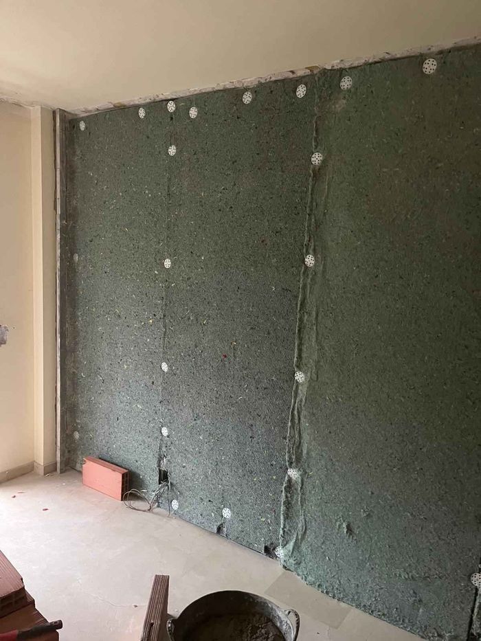 Pared verde cubierta con paneles aislantes y fijaciones en una habitación sin terminar.