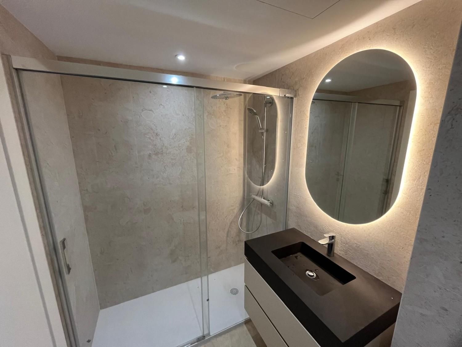 Baño moderno con ducha a ras de suelo, lavabo suspendido y espejo ovalado iluminado.